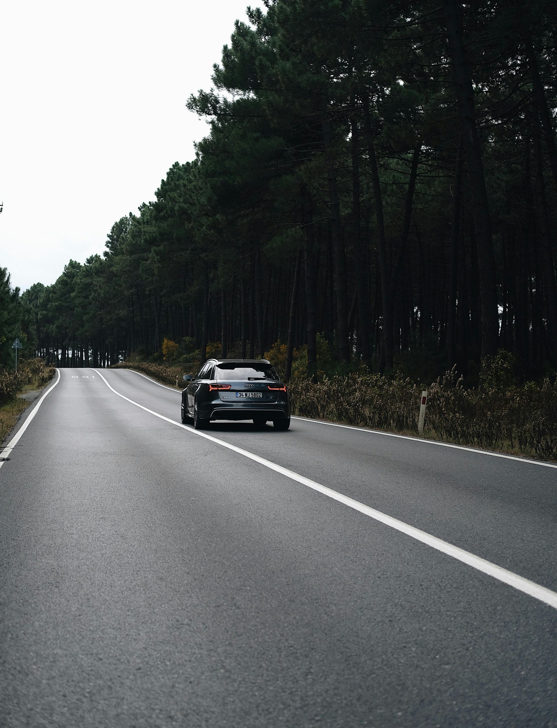 A car is driving down a road surrounded by trees.