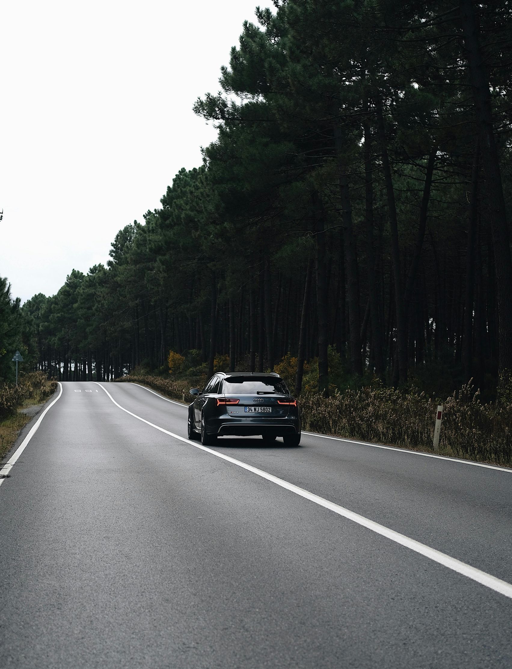 A car is driving down a road surrounded by trees.