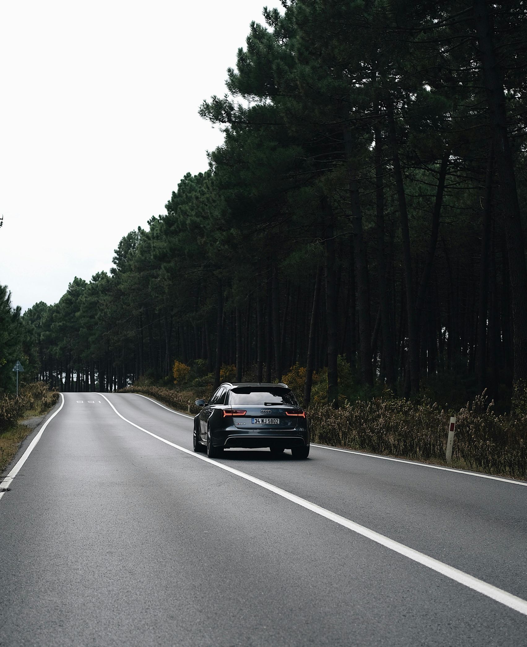 A car is driving down a road surrounded by trees.