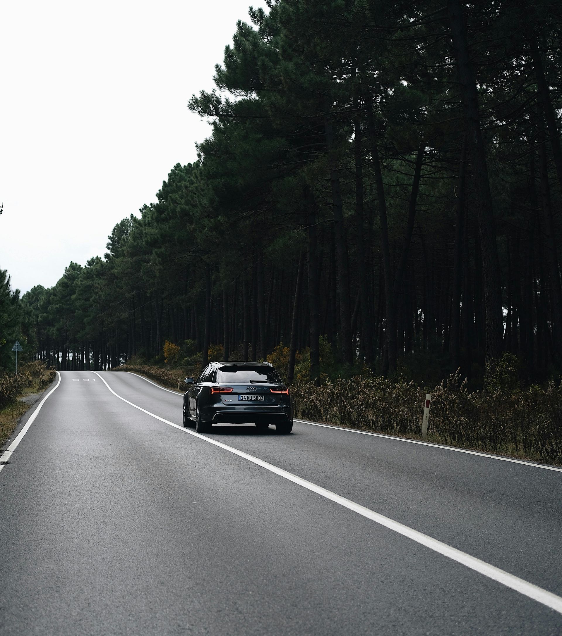 A car is driving down a road surrounded by trees.