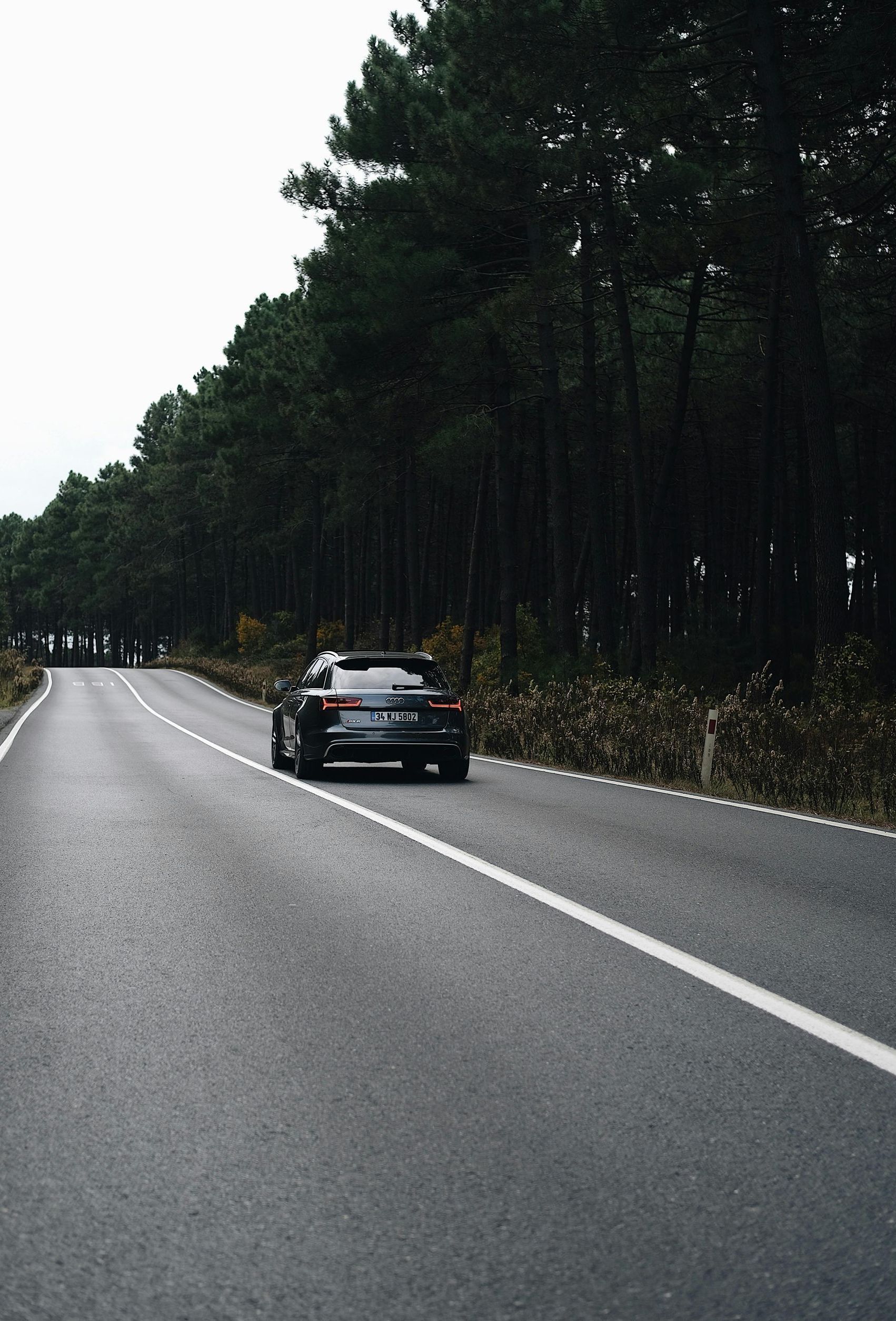 A car is driving down a road surrounded by trees.