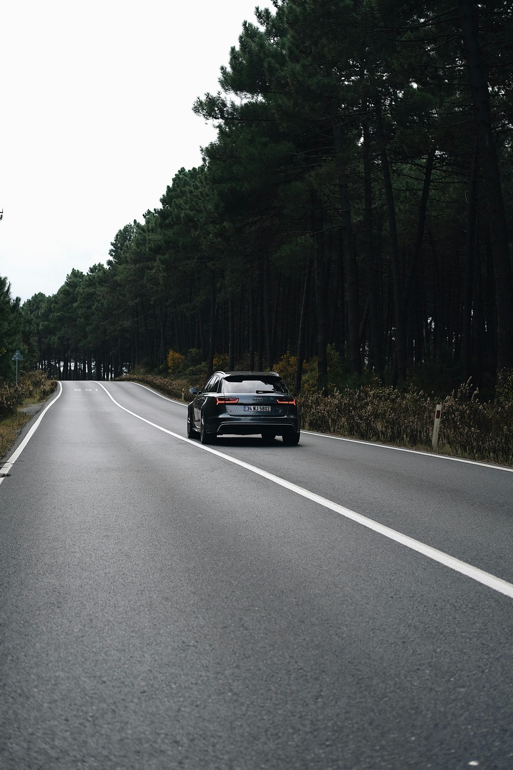 A car is driving down a road surrounded by trees.