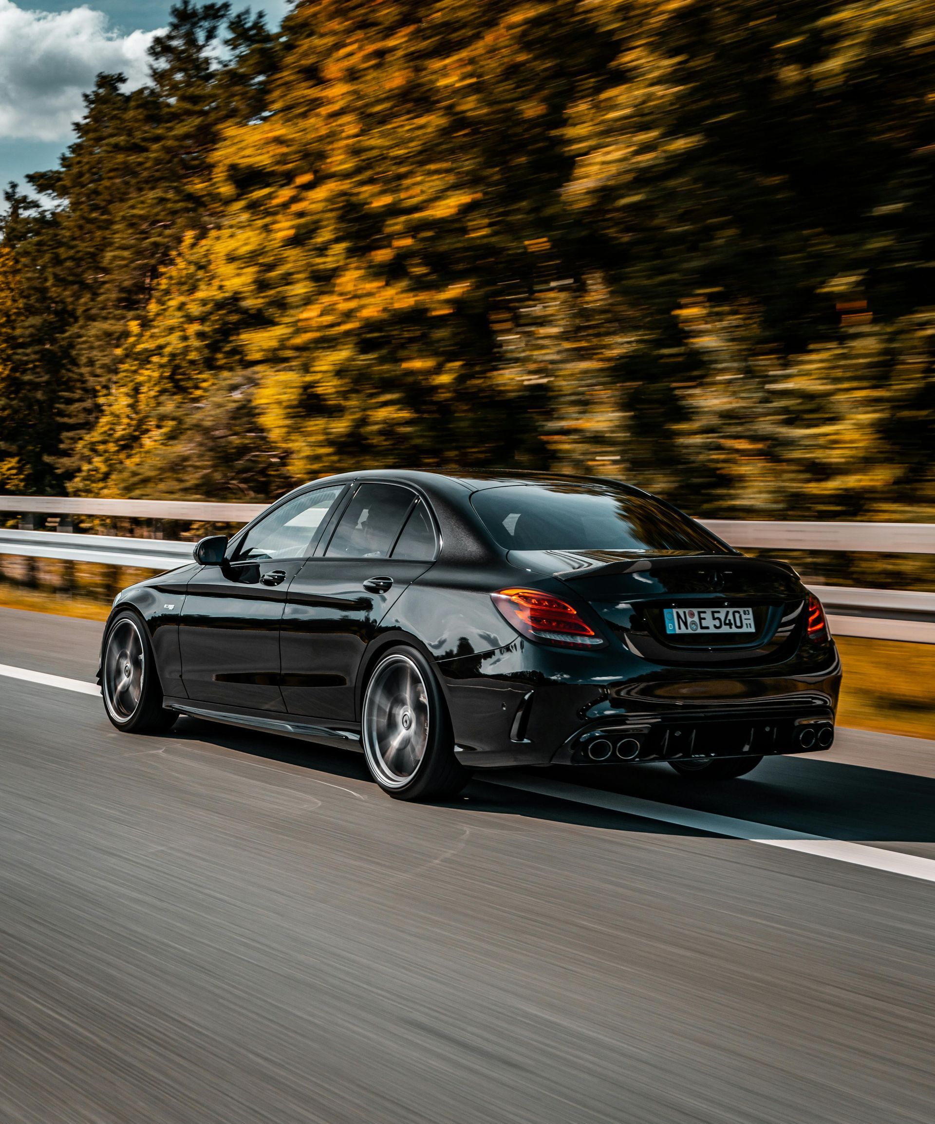 A black car is driving down a highway with trees in the background.