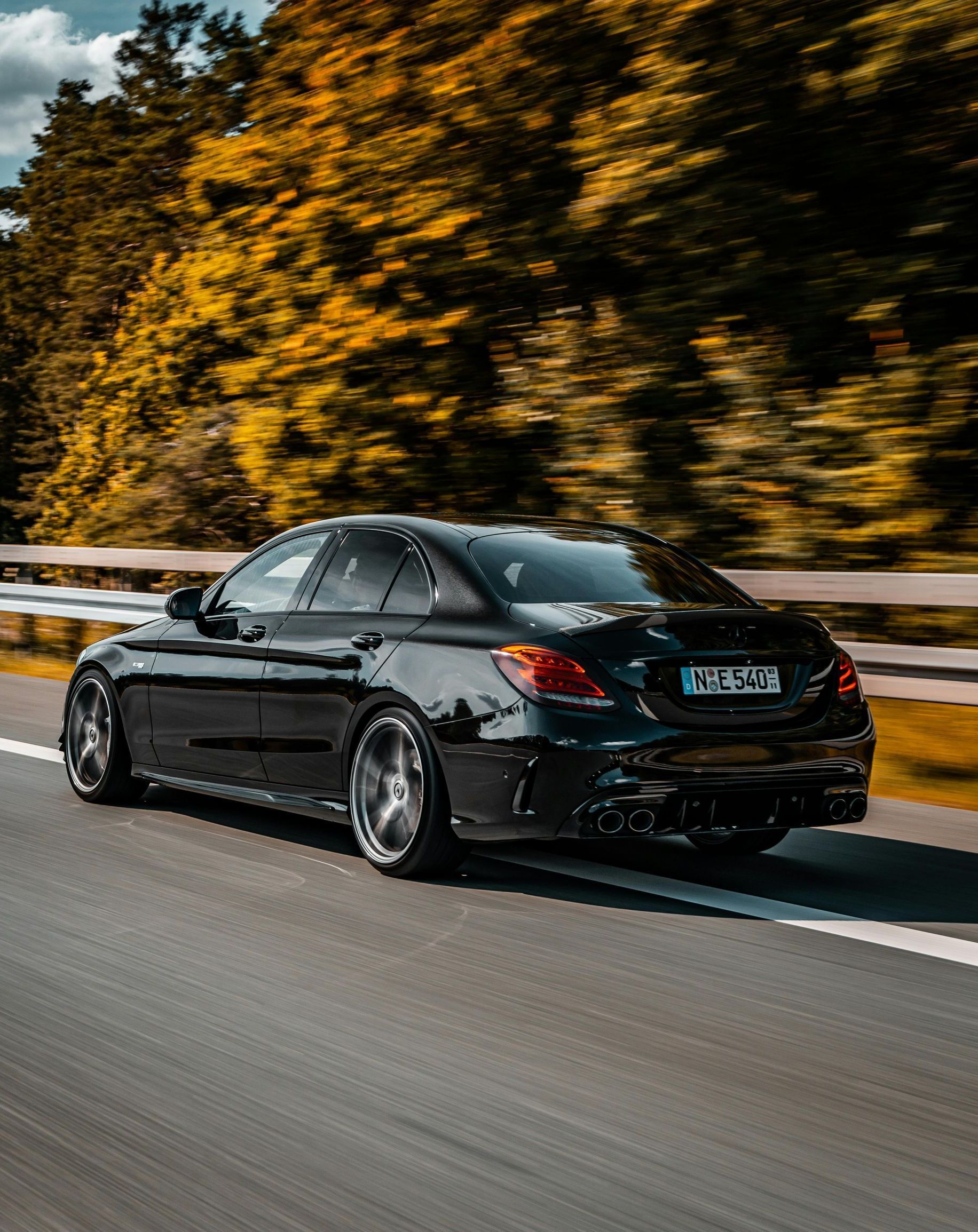 A black car is driving down a highway with trees in the background.