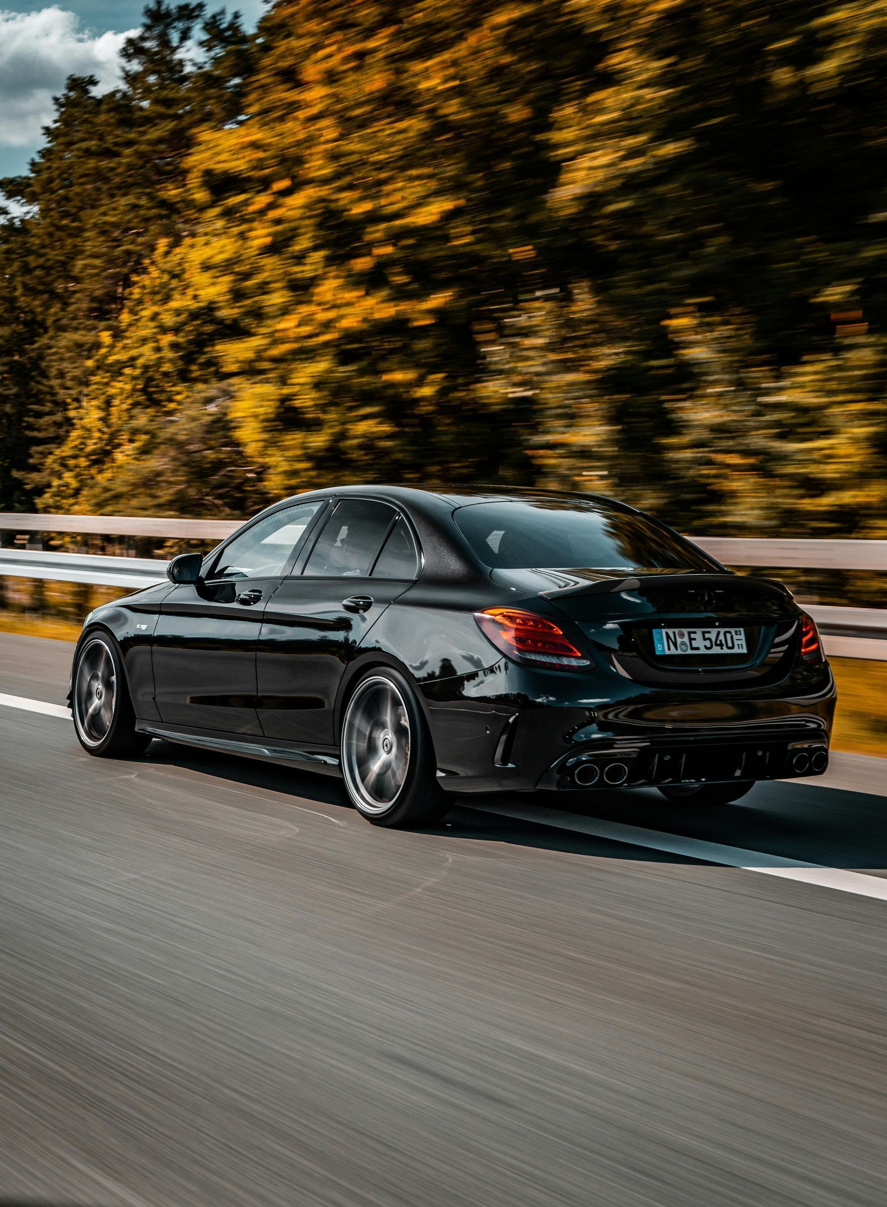 A black car is driving down a highway with trees in the background.