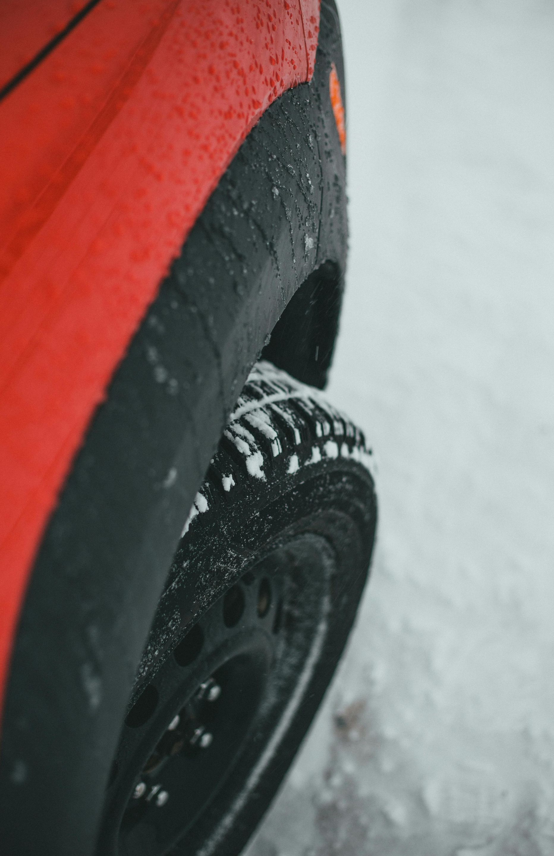 Red car tire with snow chains on a snowy road.