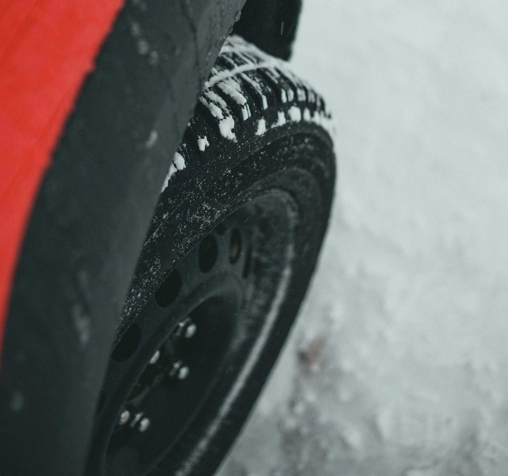Red car tire covered in snow on a winter road.