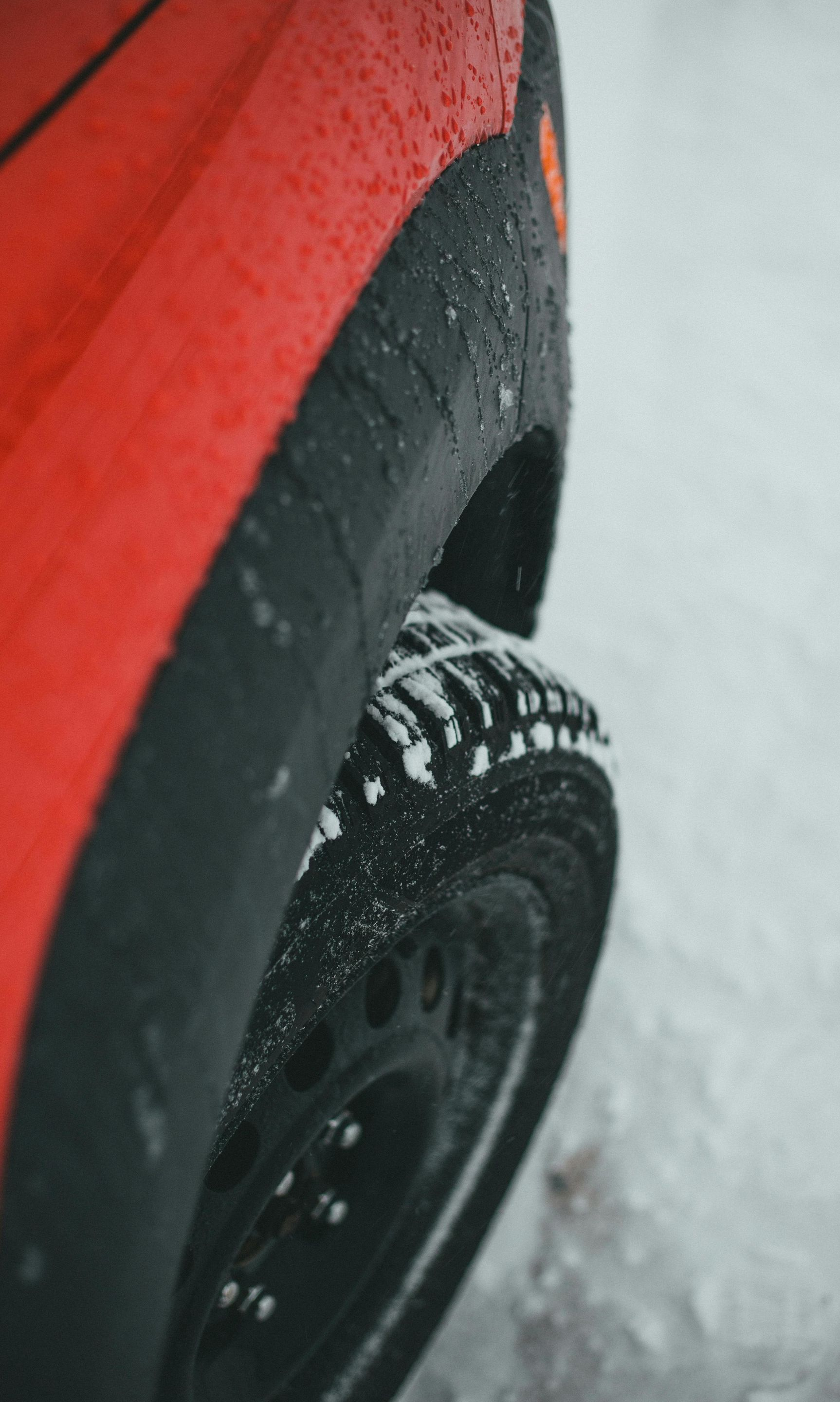 Red car tire with snow chains on a snowy road.