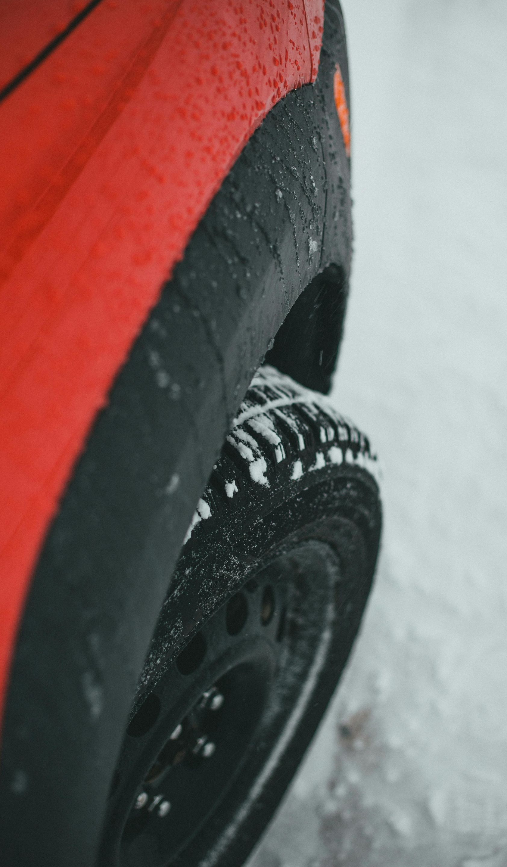 Red car tire with snow chains on a snowy road.