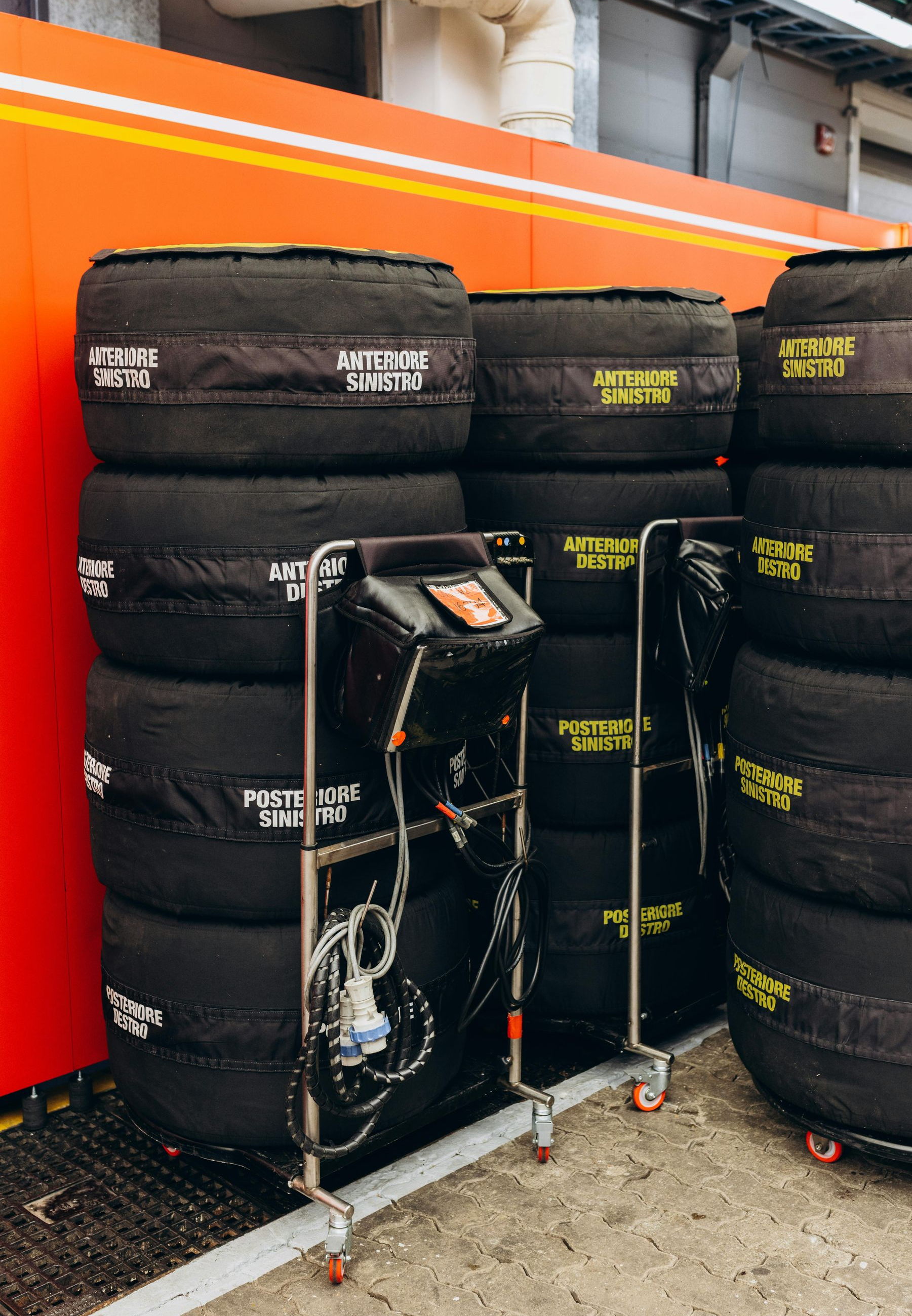 Tires with covers stacked near a cart with monitoring equipment inside a garage, possibly a race setting.