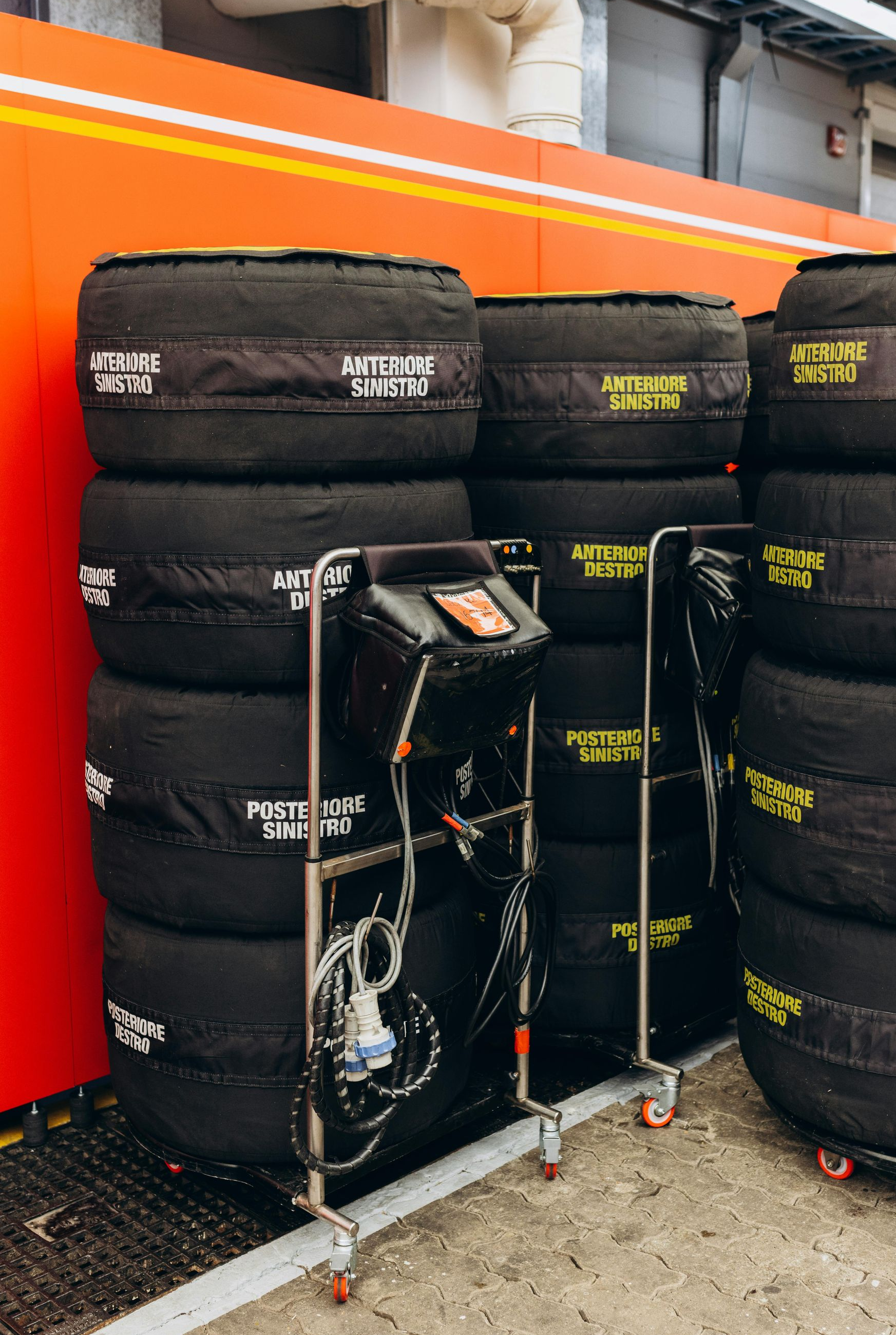 Tires with covers stacked near a cart with monitoring equipment inside a garage, possibly a race setting.