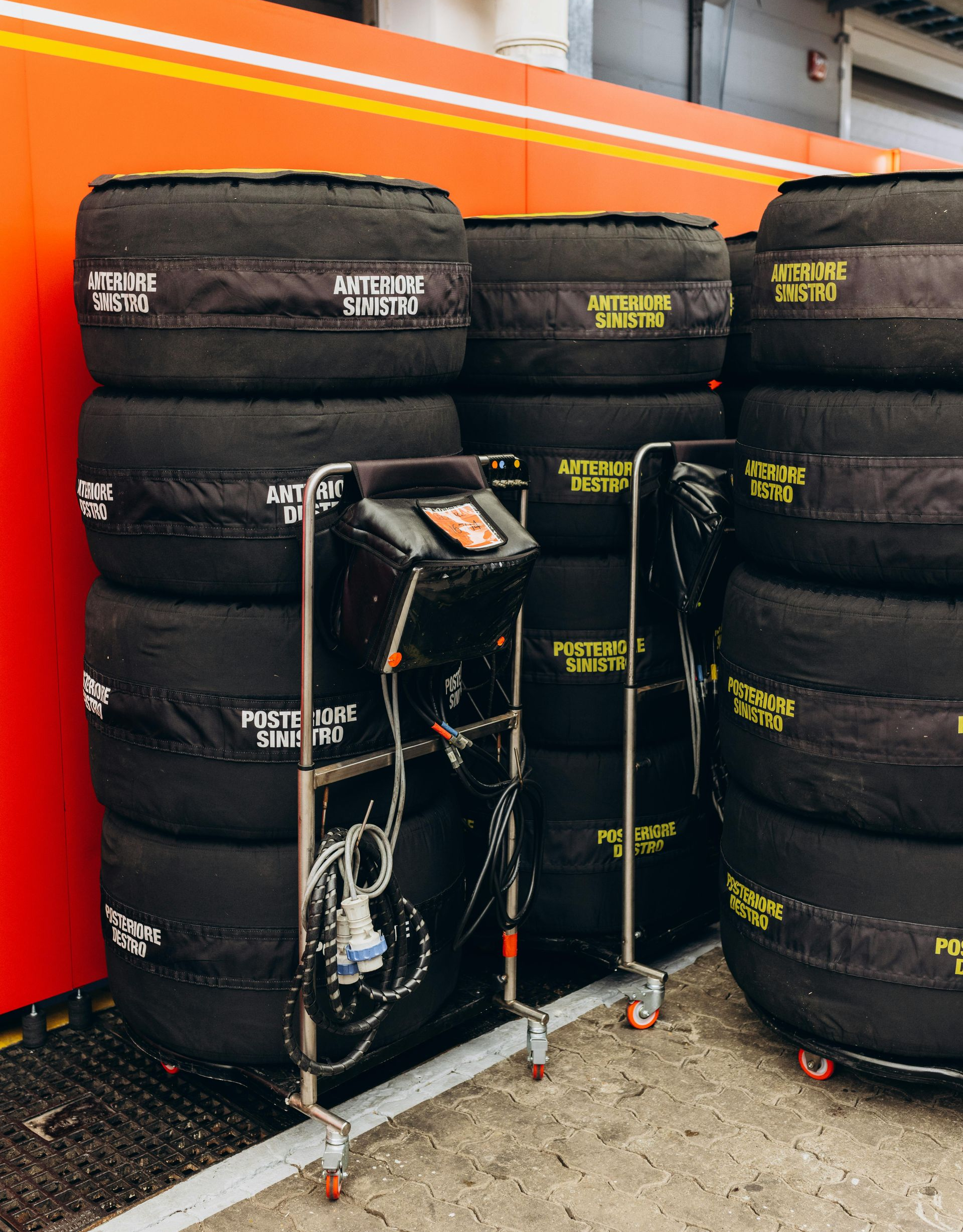 Tires with covers stacked near a cart with monitoring equipment inside a garage, possibly a race setting.