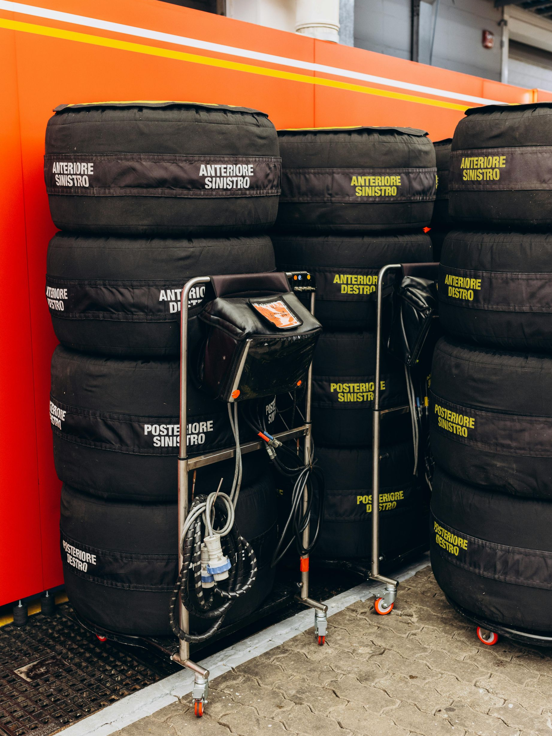 Tires with covers stacked near a cart with monitoring equipment inside a garage, possibly a race setting.