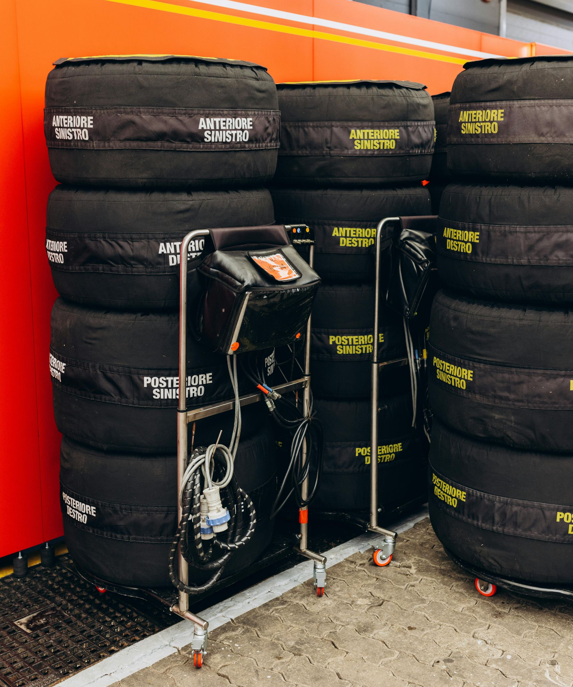 Tires with covers stacked near a cart with monitoring equipment inside a garage, possibly a race setting.