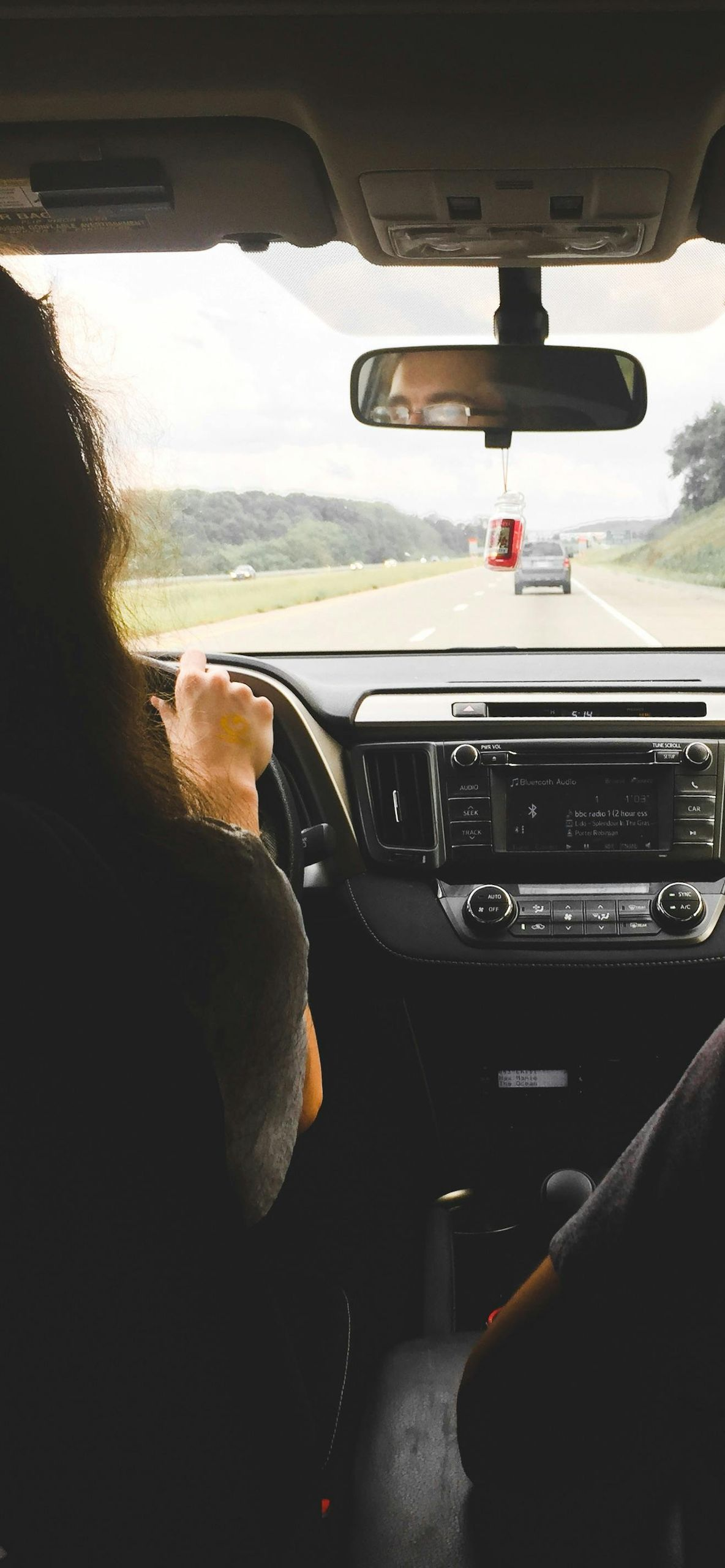 Person driving a car on a highway. View from inside the car with the dashboard and road ahead visible.