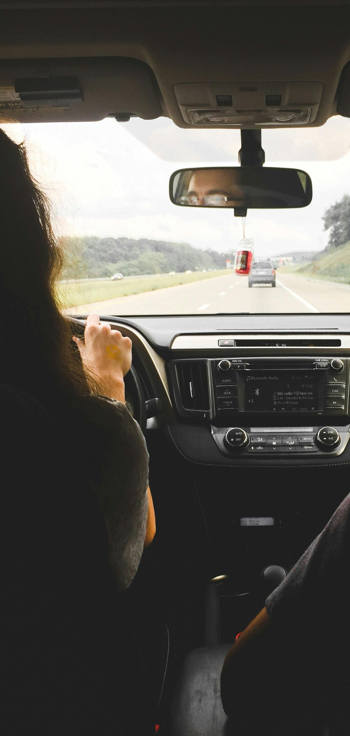 Person driving a car on a highway. View from inside the car with the dashboard and road ahead visible.