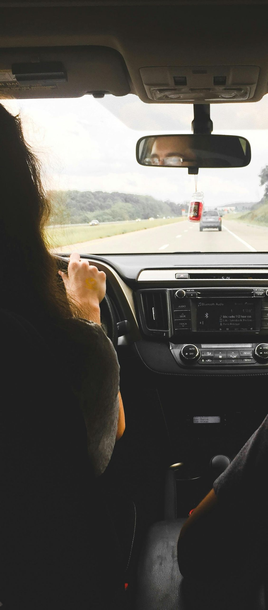 Person driving a car on a highway. View from inside the car with the dashboard and road ahead visible.