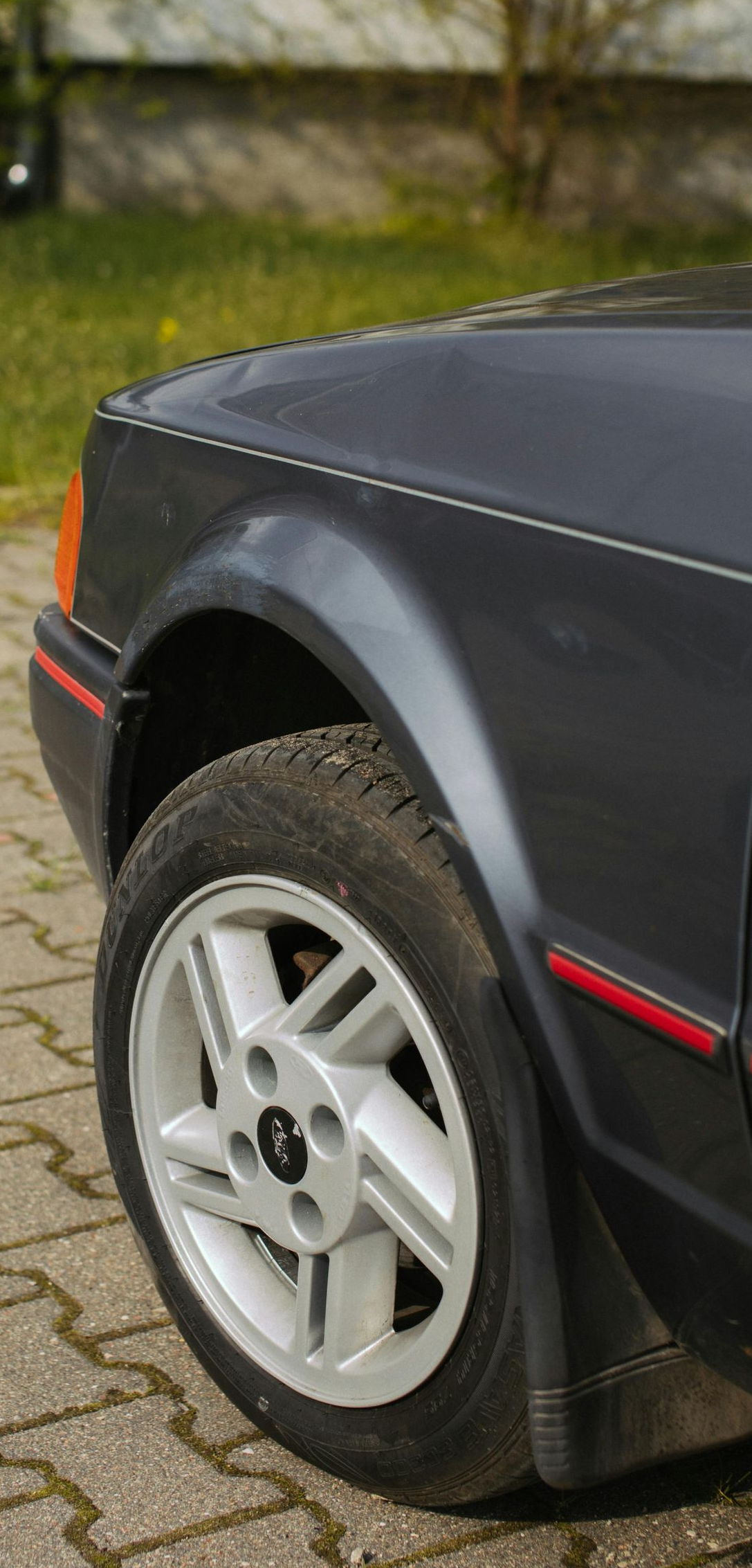 Front quarter view of a dark gray car with a silver rim. Red detail along the car's body.