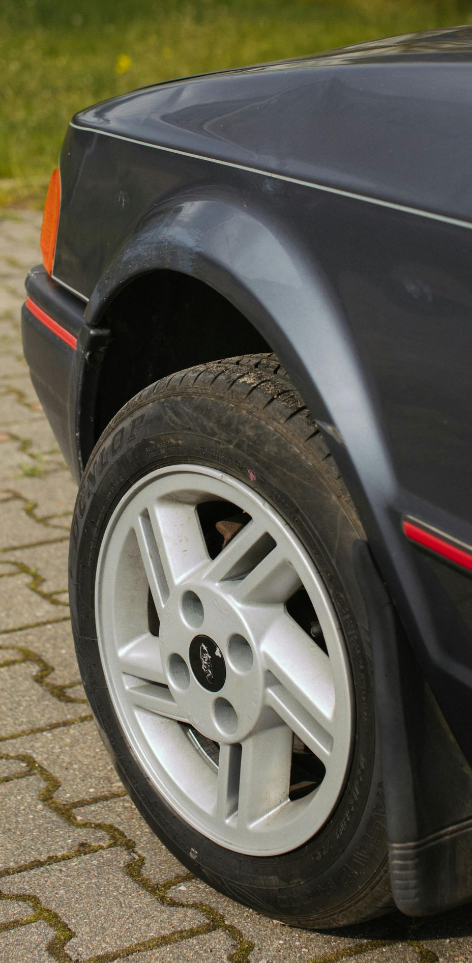 Dark grey Ford Escort front quarter panel, wheel on brick pavement.