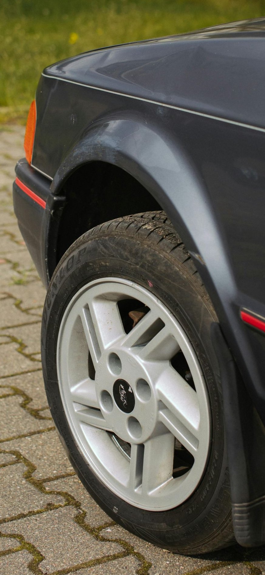 Dark grey Ford Escort front quarter panel, wheel on brick pavement.