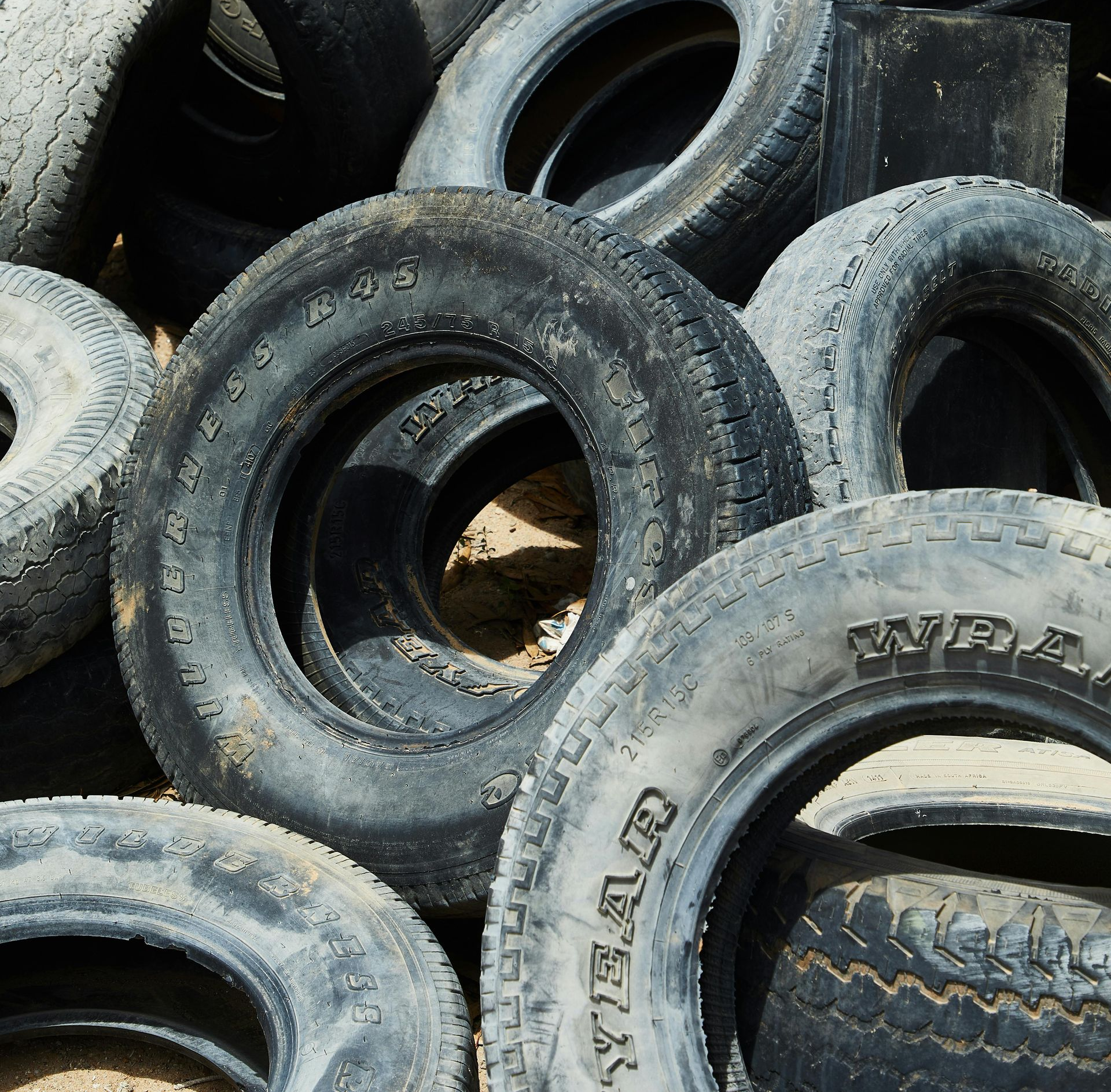A pile of weathered, black rubber tires stacked on sandy ground.