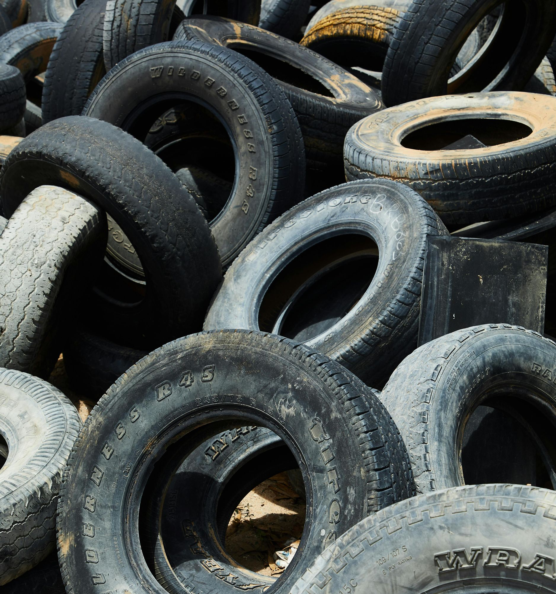 A pile of weathered, black rubber tires stacked on sandy ground.