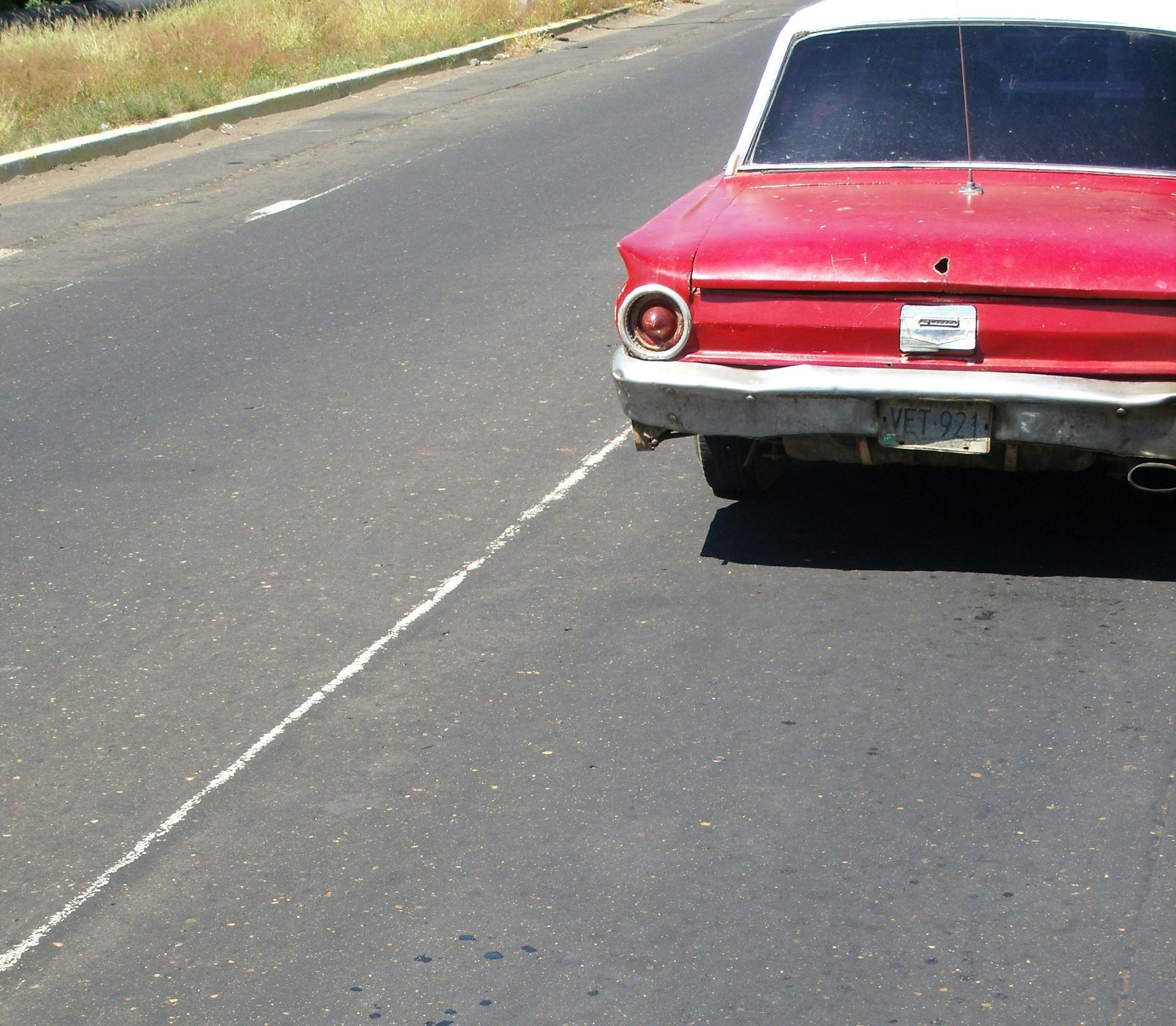 A red vintage car parked on the shoulder of an asphalt road.