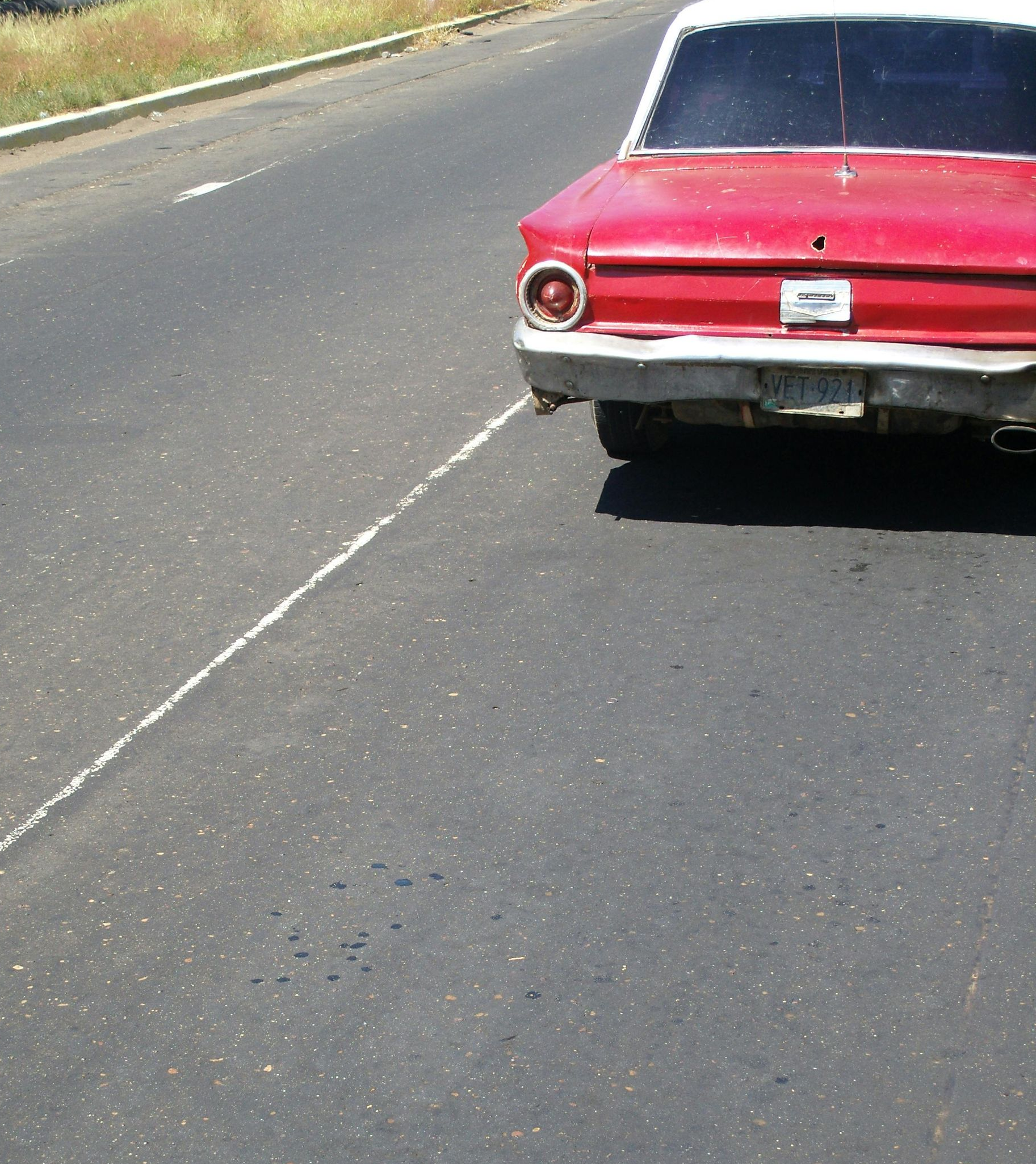 A red vintage car parked on the shoulder of an asphalt road.