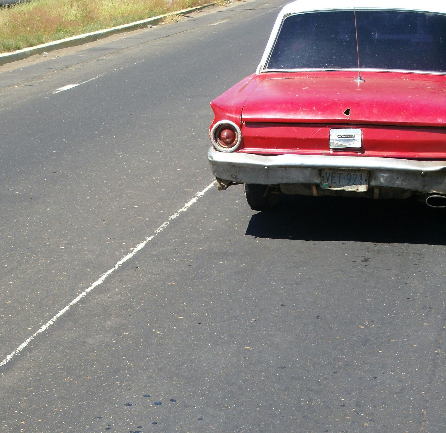 A red vintage car parked on the shoulder of an asphalt road.
