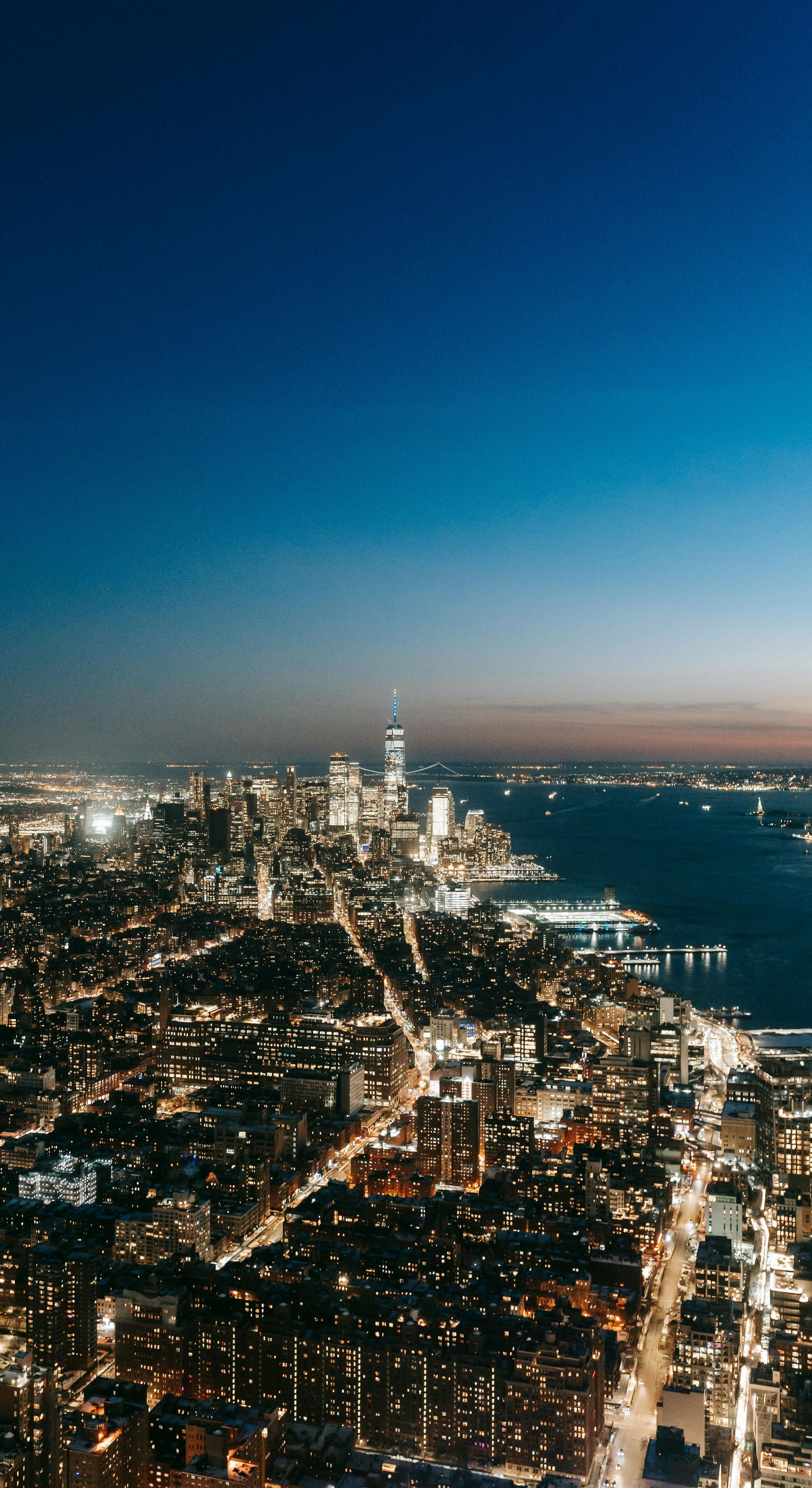 Night view of a cityscape with bright lights, a river, and a dark blue sky.
