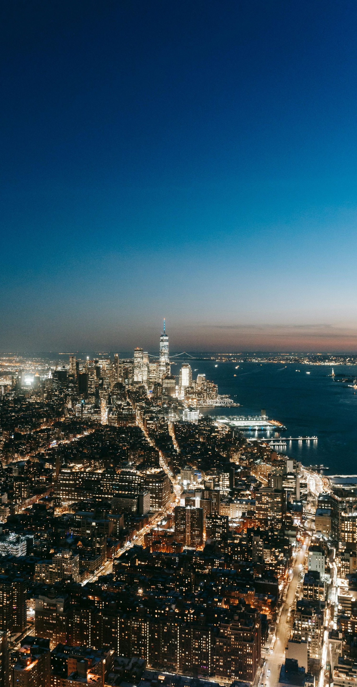 Night view of a cityscape with bright lights, a river, and a dark blue sky.