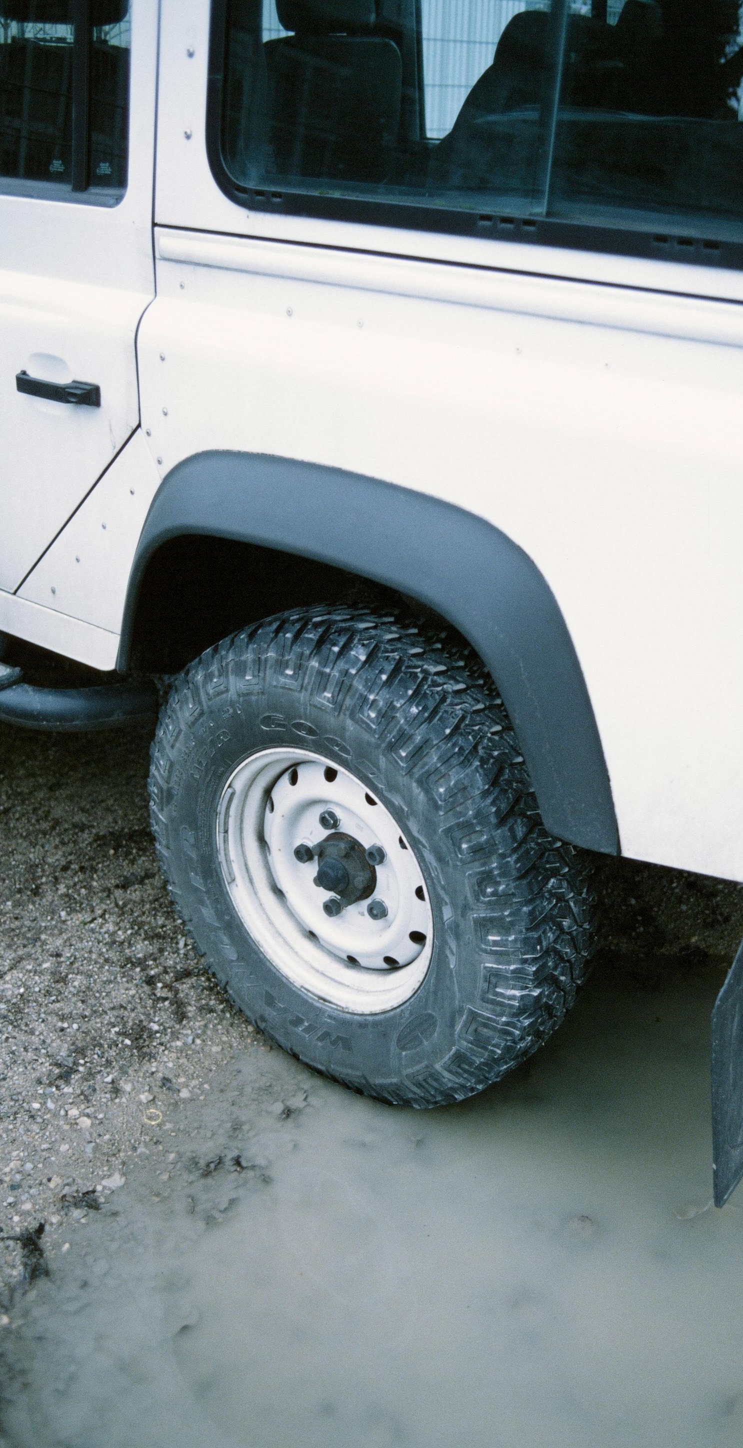 White off-road vehicle's rear wheel in muddy water, black fender flares.