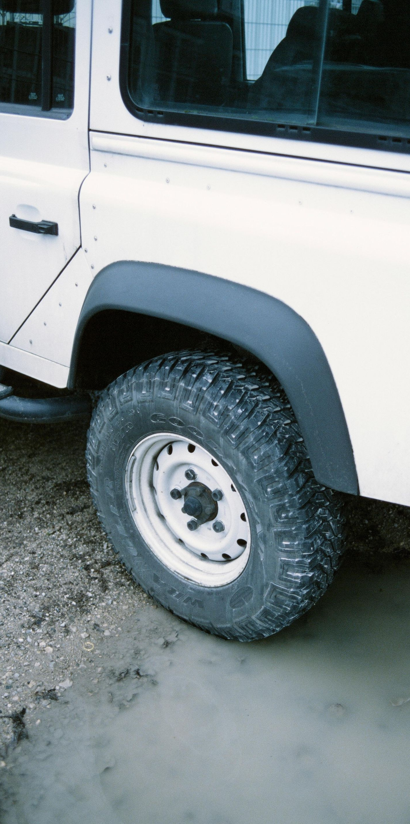 White off-road vehicle's rear wheel in muddy water, black fender flares.