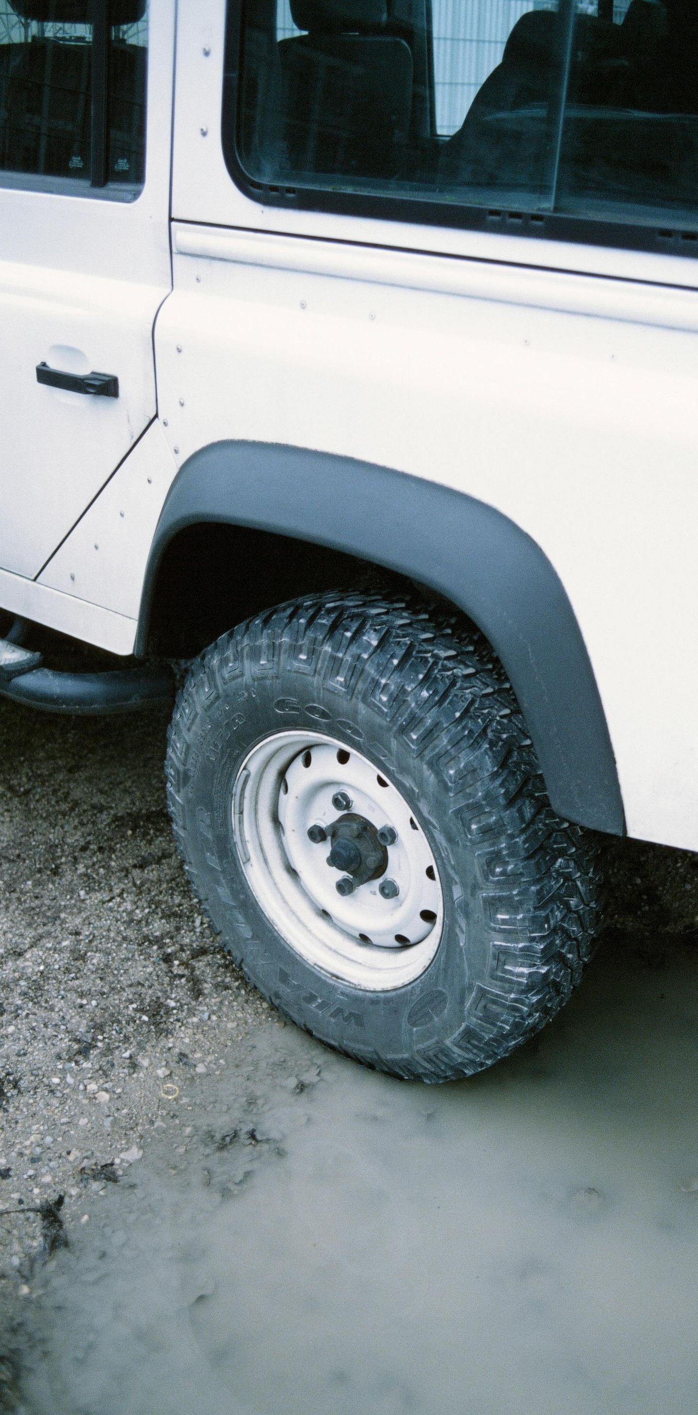 White off-road vehicle's rear wheel in muddy water, black fender flares.