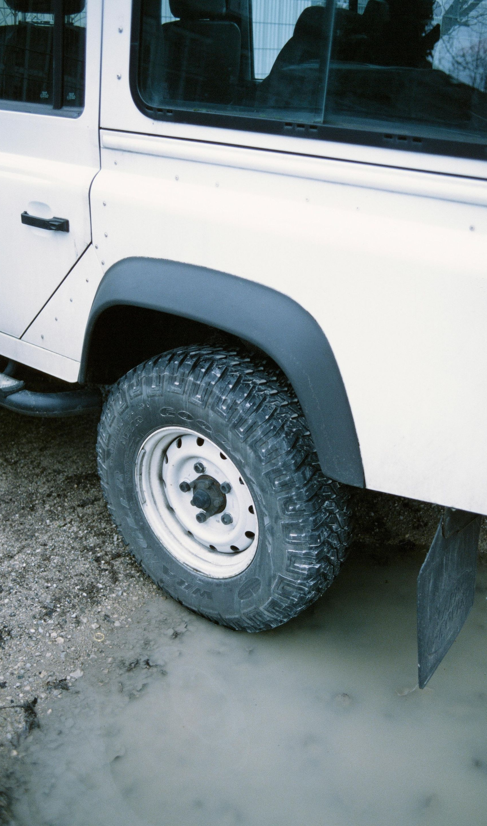 White off-road vehicle's rear wheel in muddy water, black fender flares.