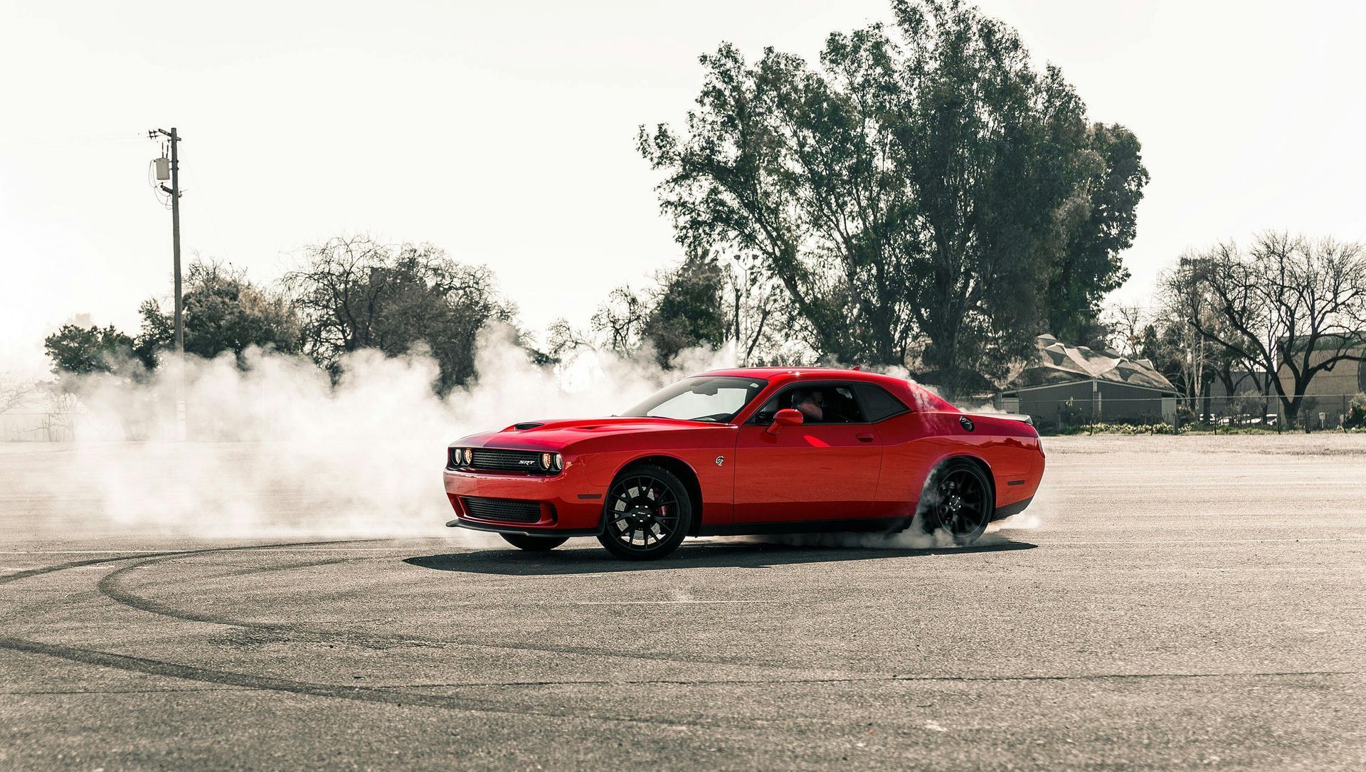 Red Dodge Challenger drifting on a paved surface, creating a cloud of white smoke.
