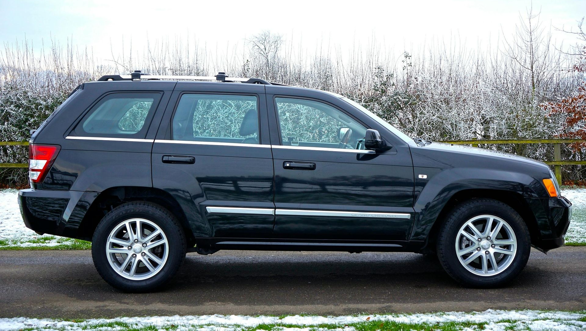 Dark gray Jeep Grand Cherokee parked on a road next to a snowy patch of grass and bushes.
