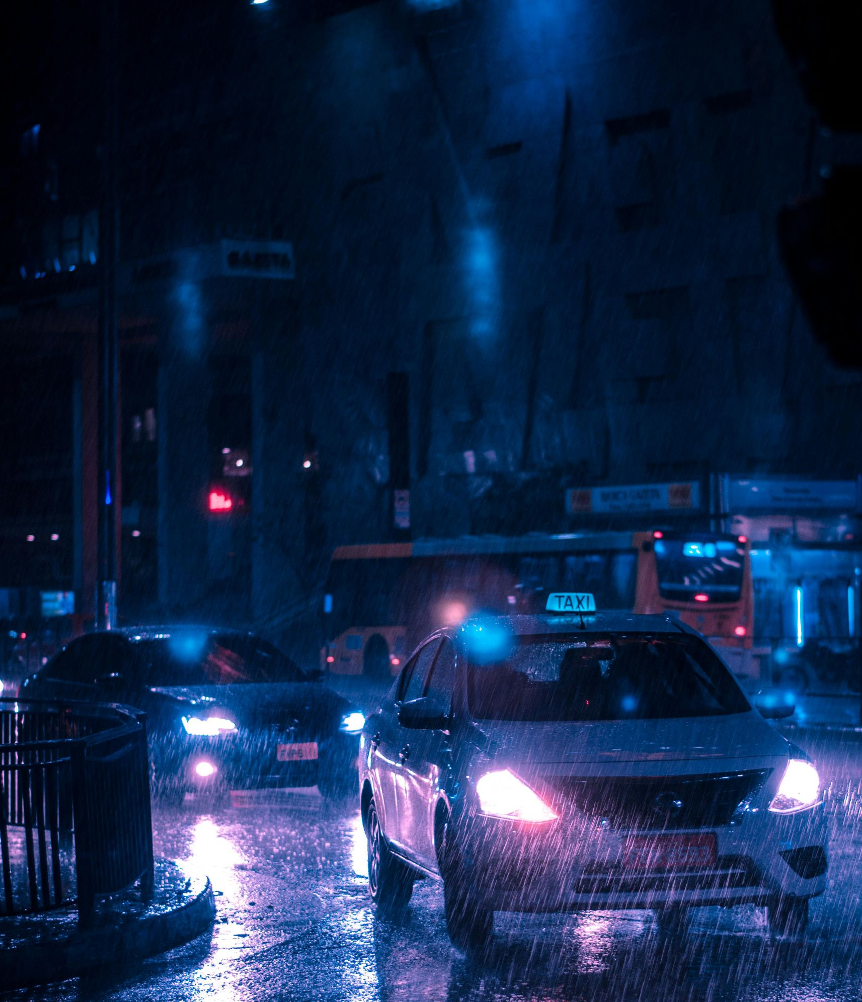 Cars driving on a wet city street at night. Rain reflects the blue and pink streetlights.