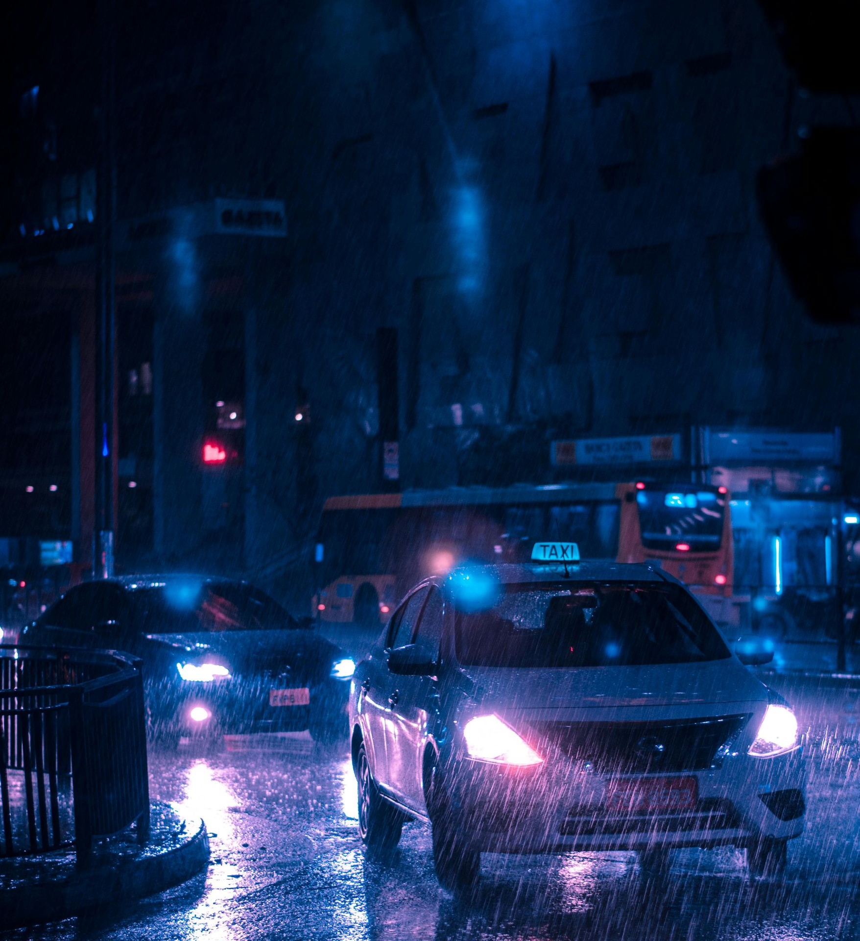 Cars driving on a wet city street at night. Rain reflects the blue and pink streetlights.