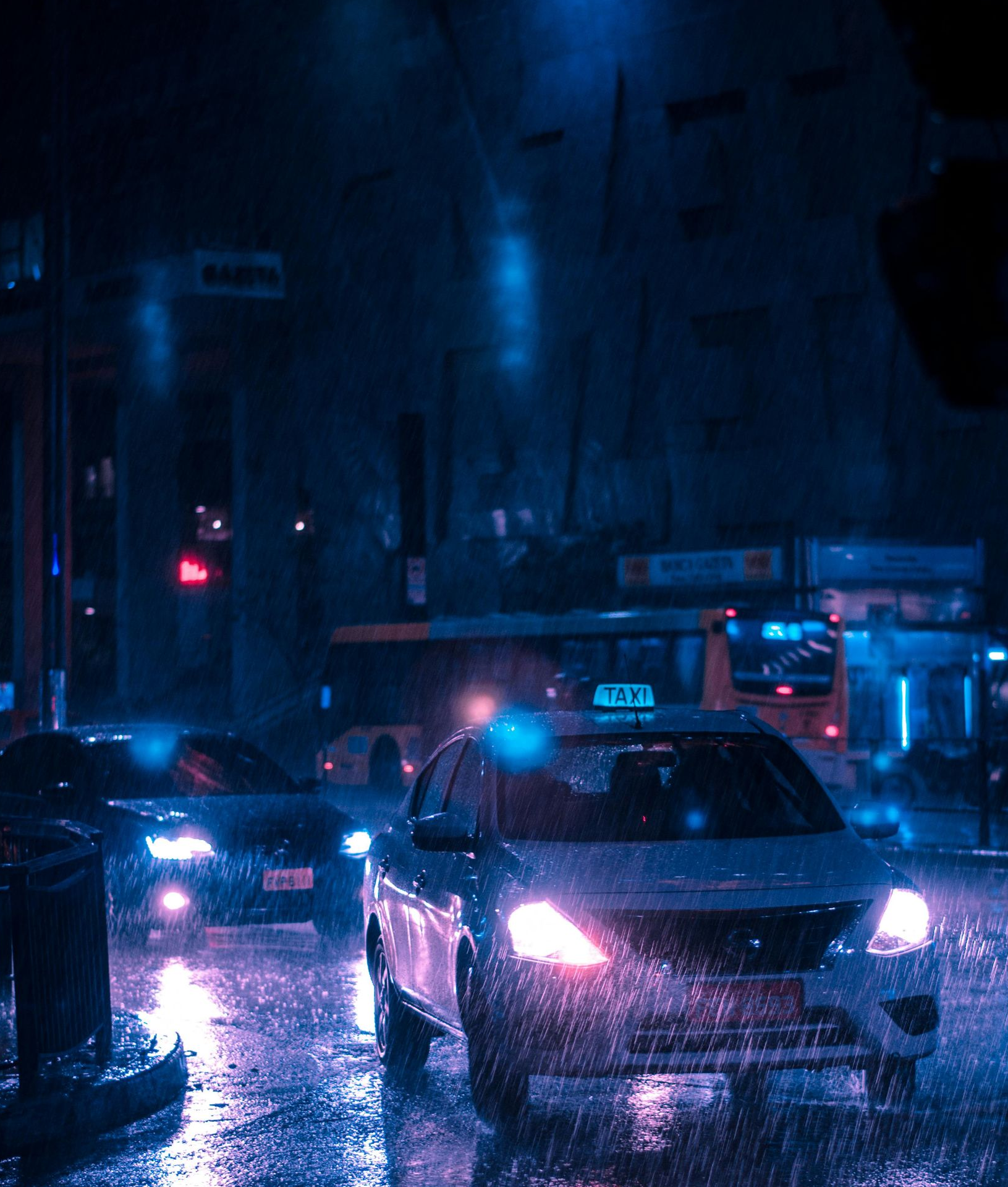 Cars driving on a wet city street at night. Rain reflects the blue and pink streetlights.