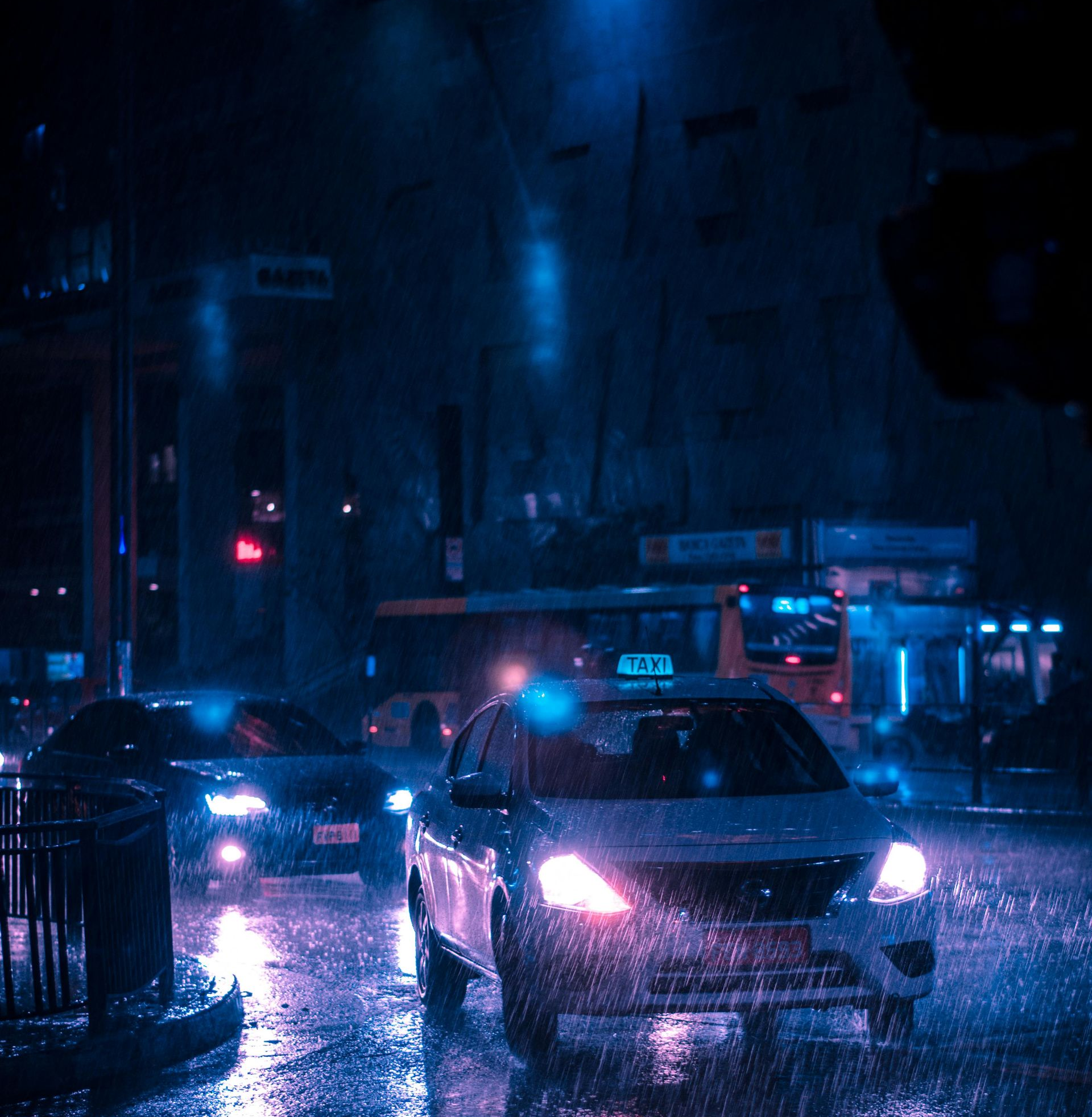 Cars driving on a wet city street at night. Rain reflects the blue and pink streetlights.