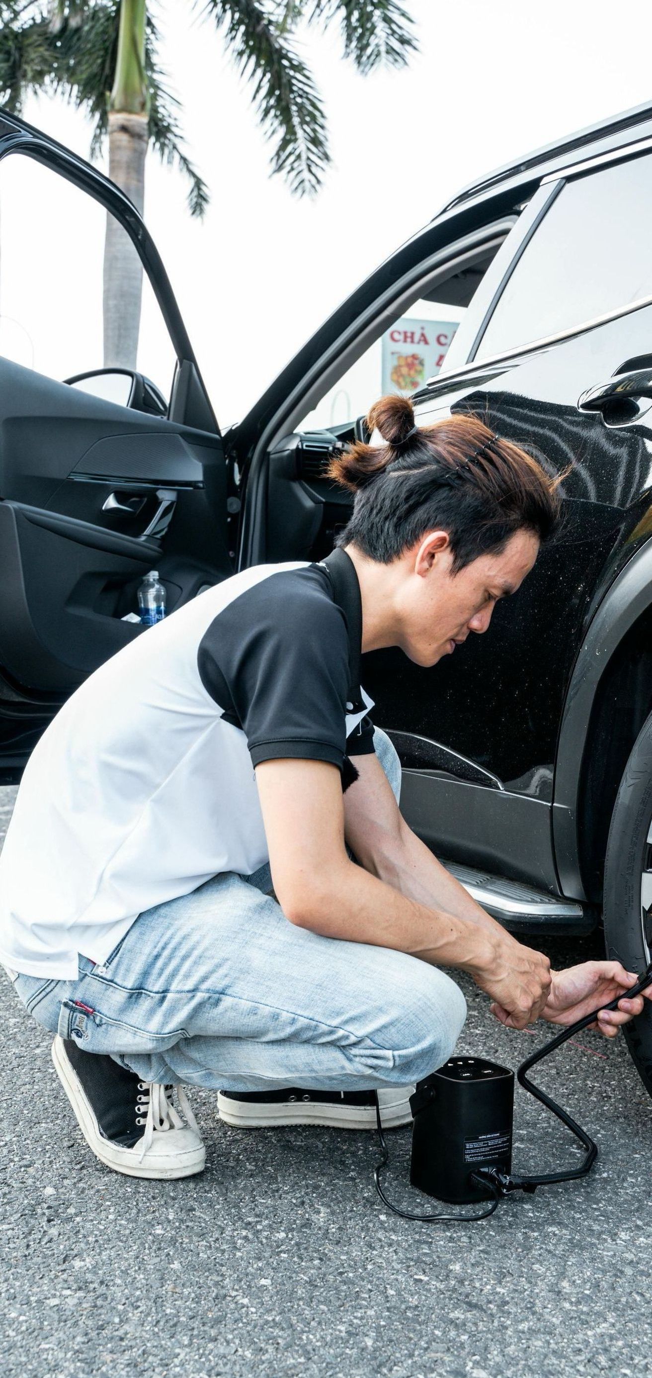 A man is kneeling down next to a car to inflate a tire.
