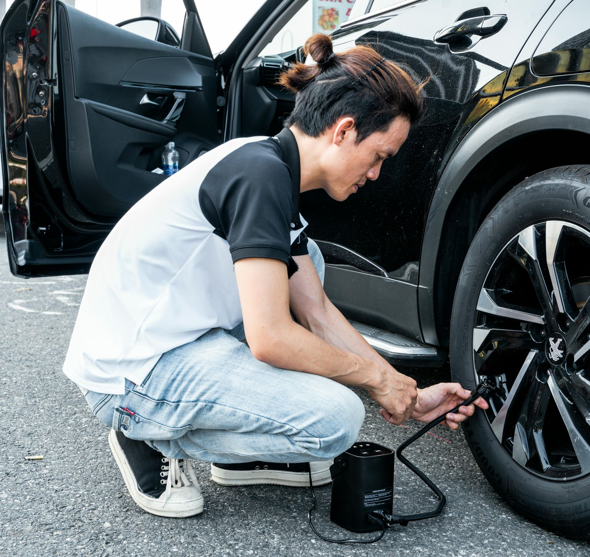 Man inflating car tire with a black air pump; vehicle door open.