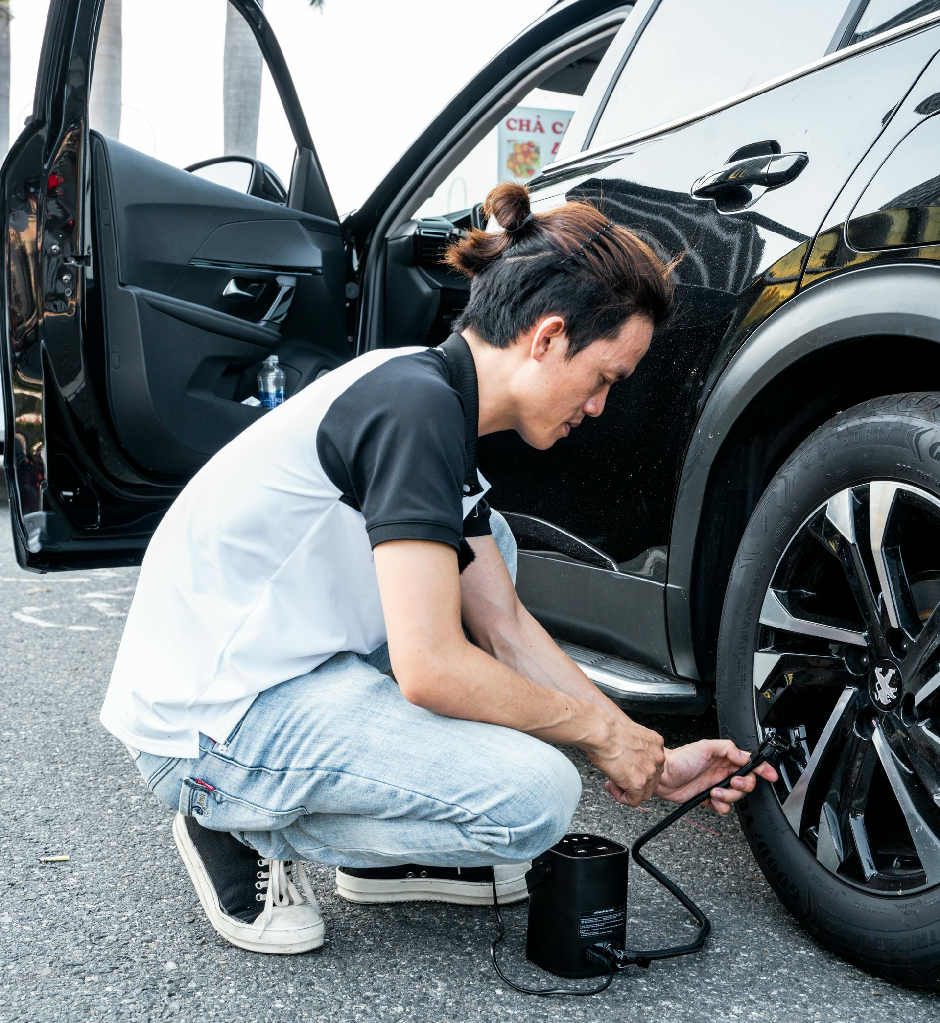 Man inflating car tire with a black air pump; vehicle door open.