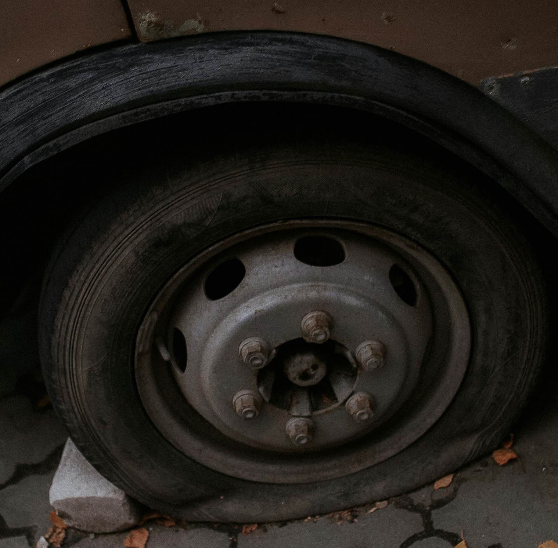 Flat tire on a vehicle's wheel, resting on a concrete block, in an outdoor setting.