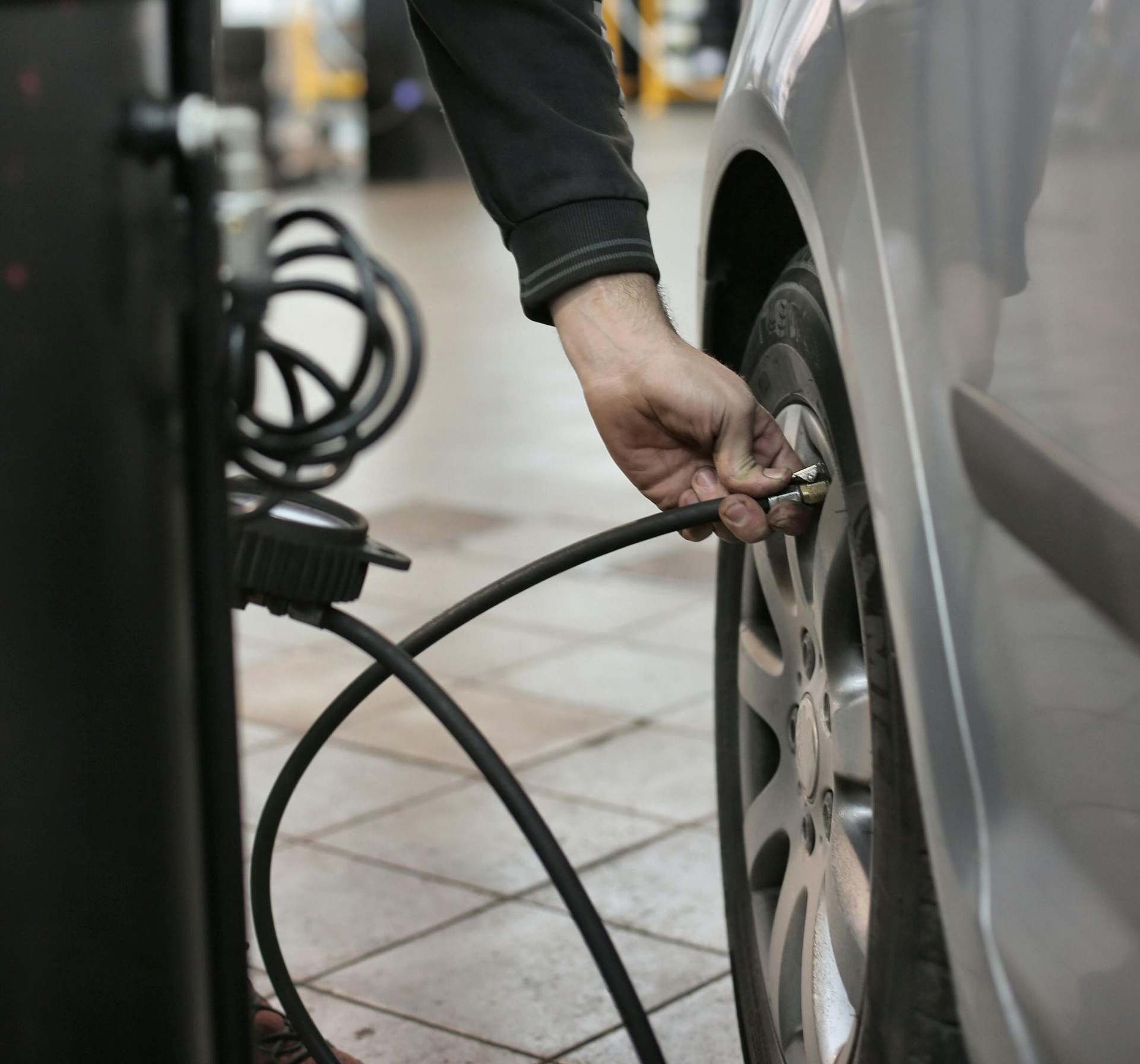 Person inflating a car tire with an air compressor in a garage.