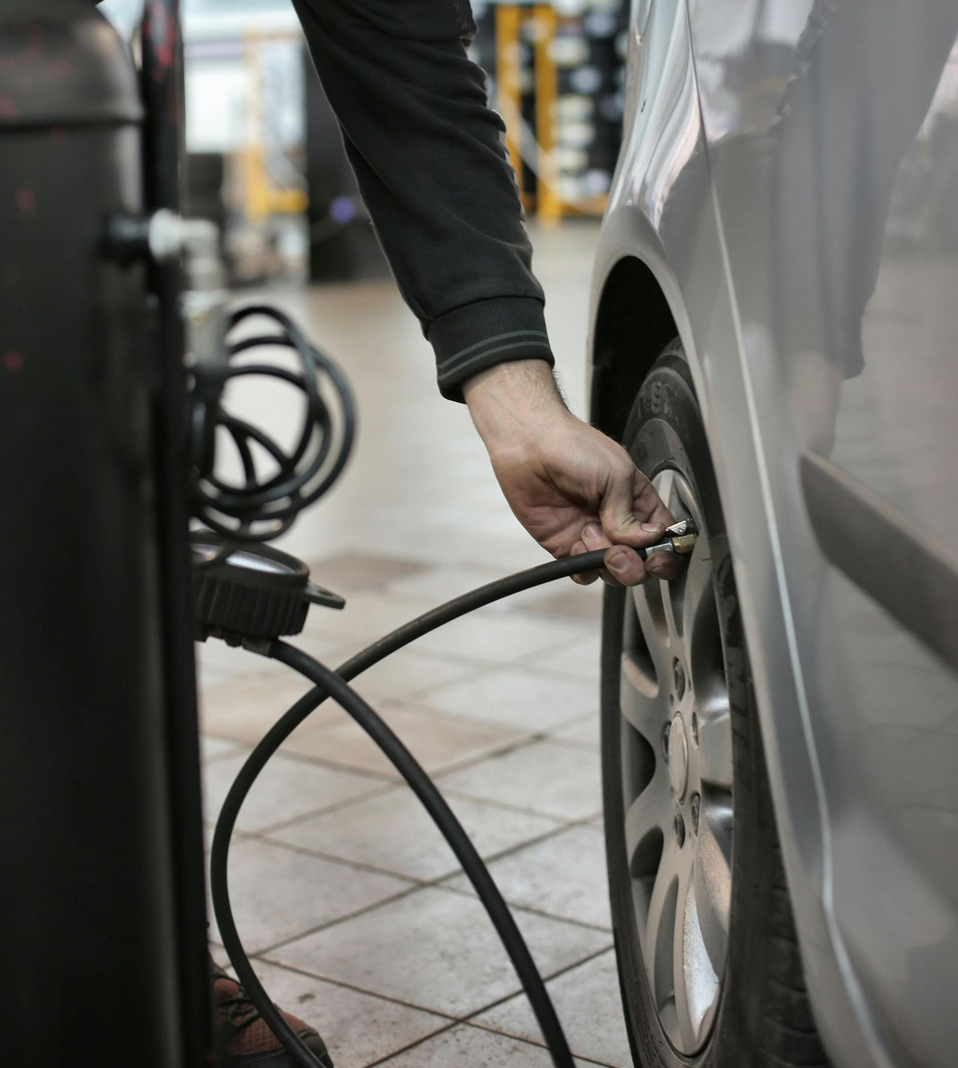 Person inflating a car tire with an air compressor in a garage.