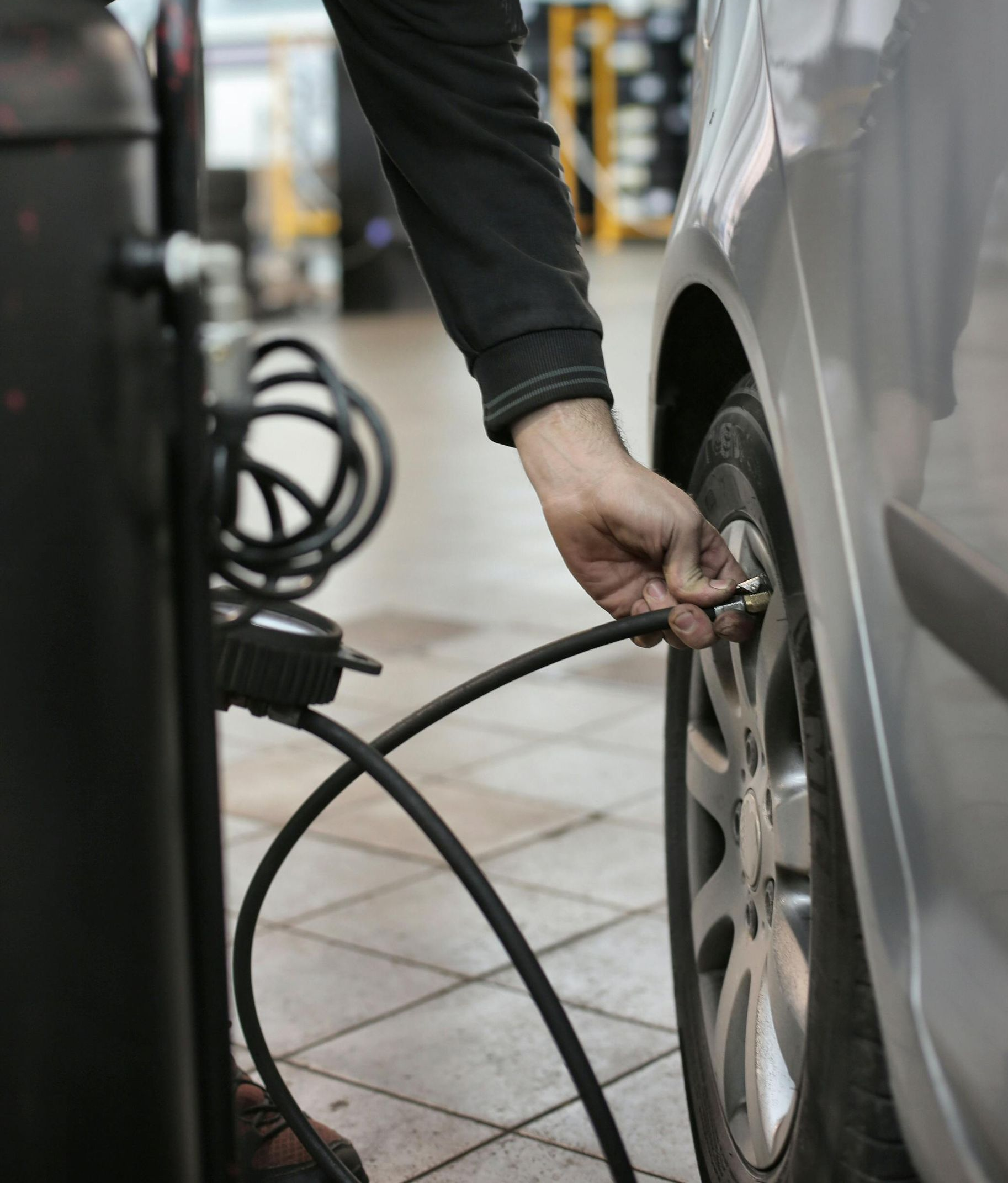 Person inflating a car tire with an air compressor in a garage.