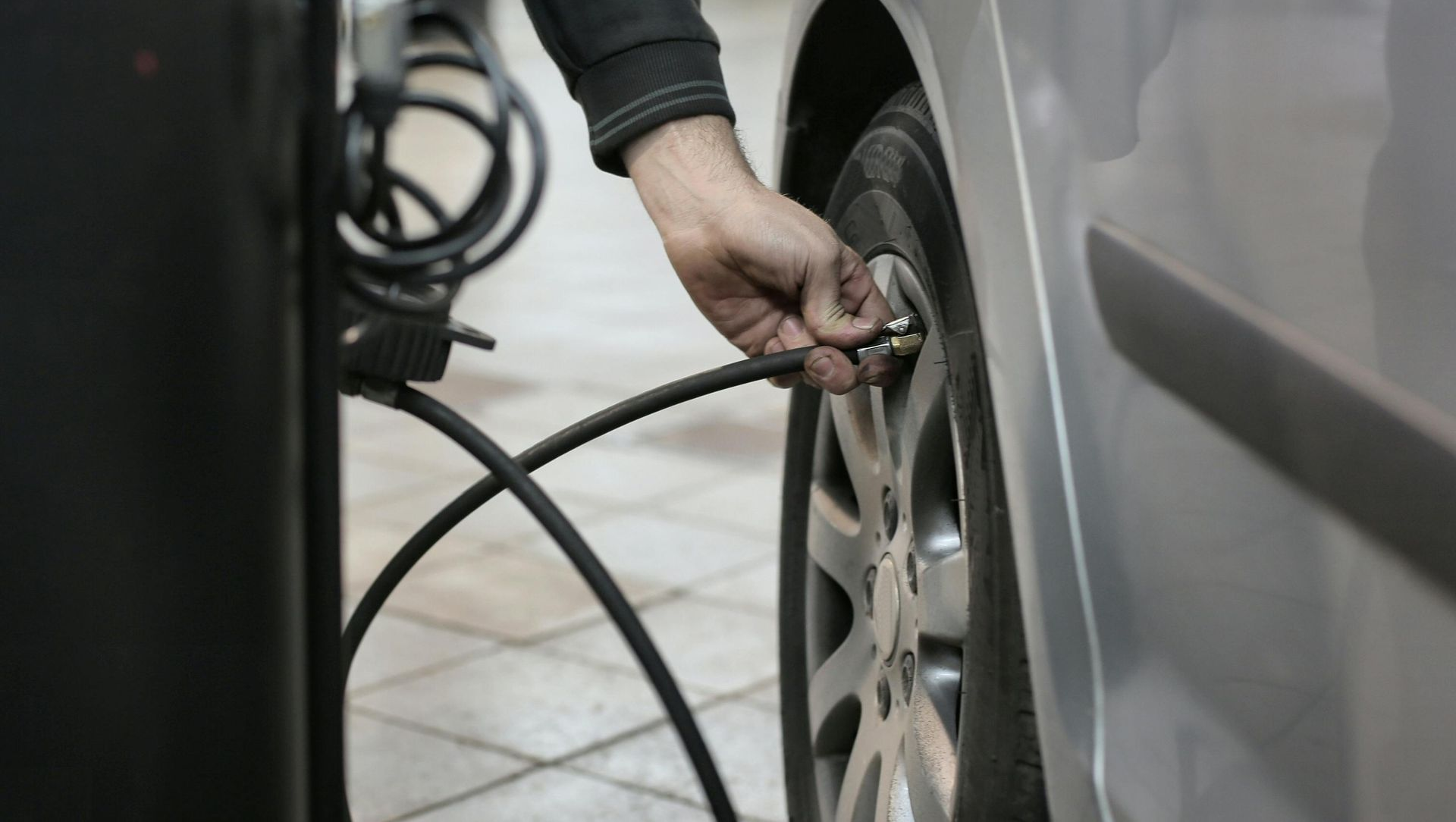 Person inflating a car tire with an air compressor in a garage.