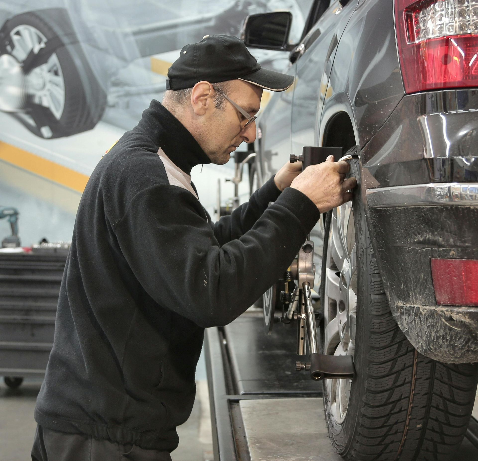 Mechanic aligning car's rear tire on a lift in a shop, using tools.